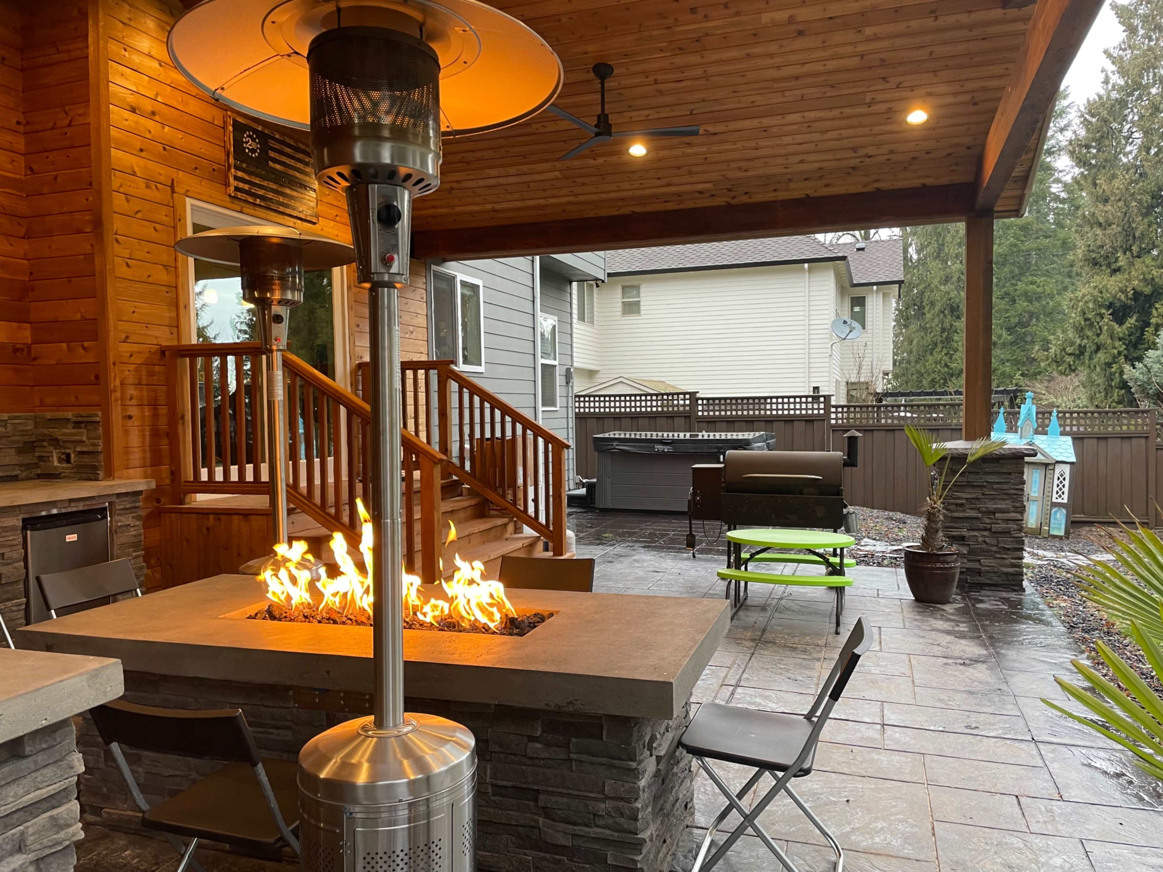 A covered patio area with a stone fire pit, outdoor seating, and a hot tub in the background.