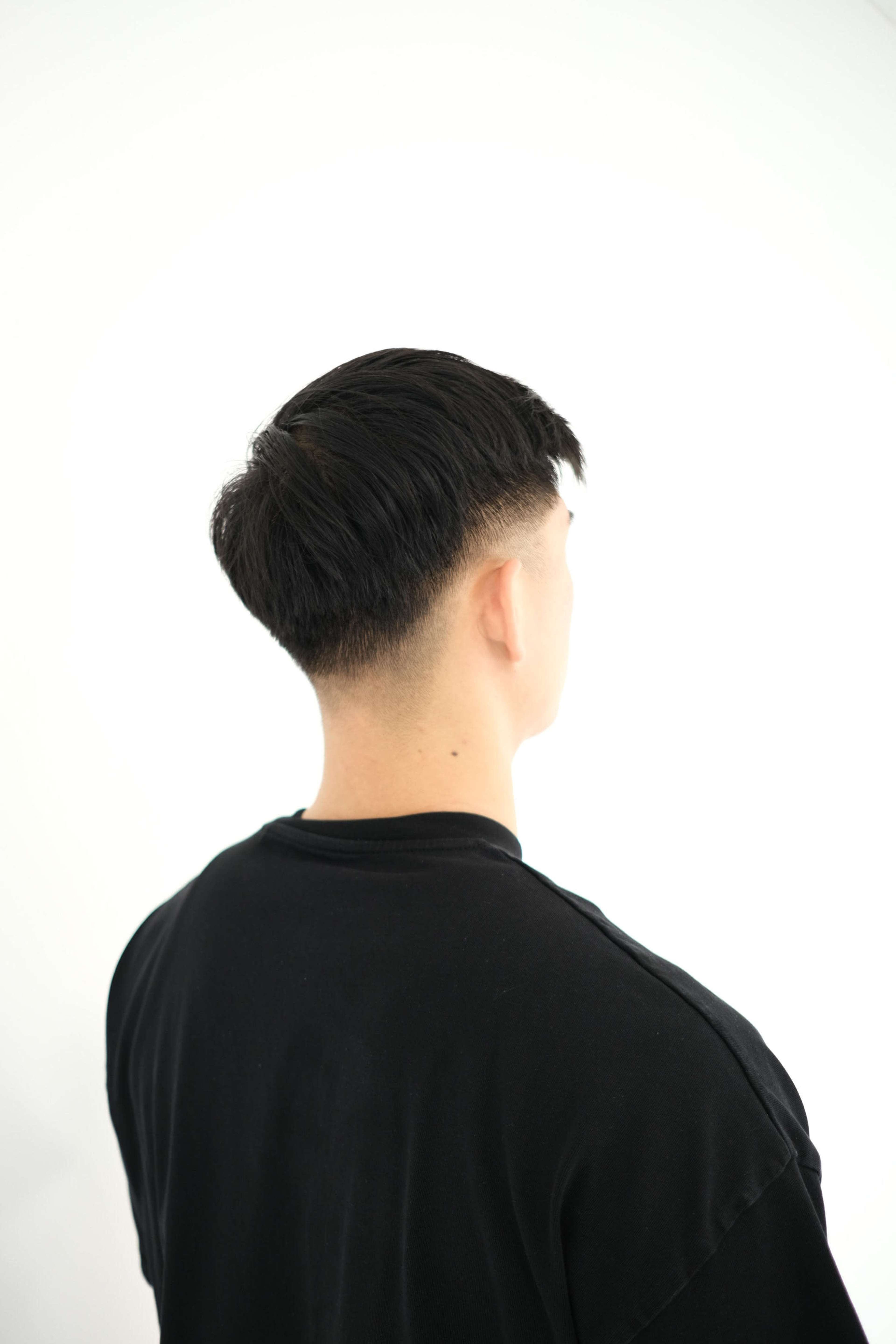 A person with short hair is seen from behind, facing a plain white background.