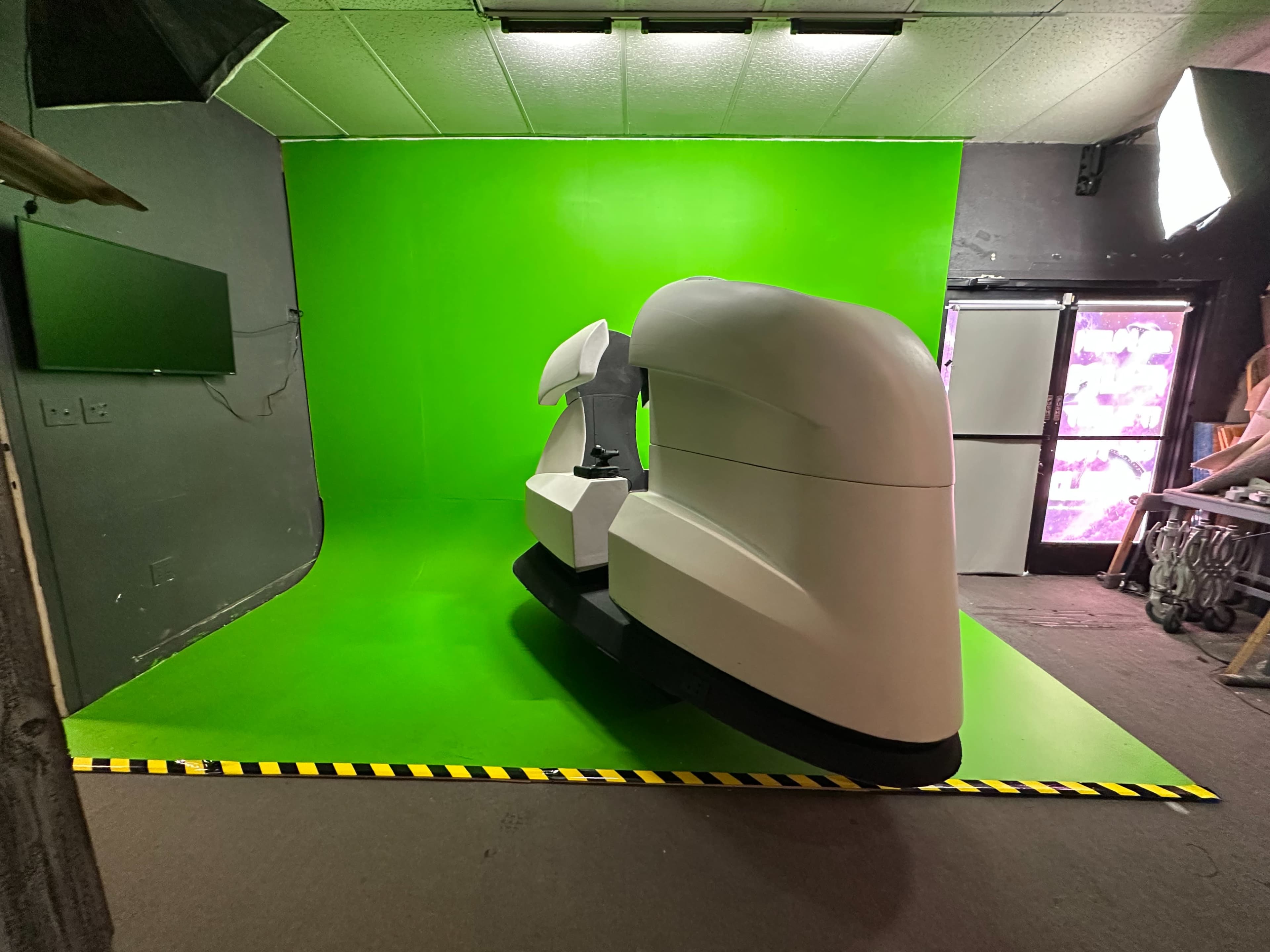 The image shows a large white piece of equipment positioned on a bright green backdrop in a studio environment.