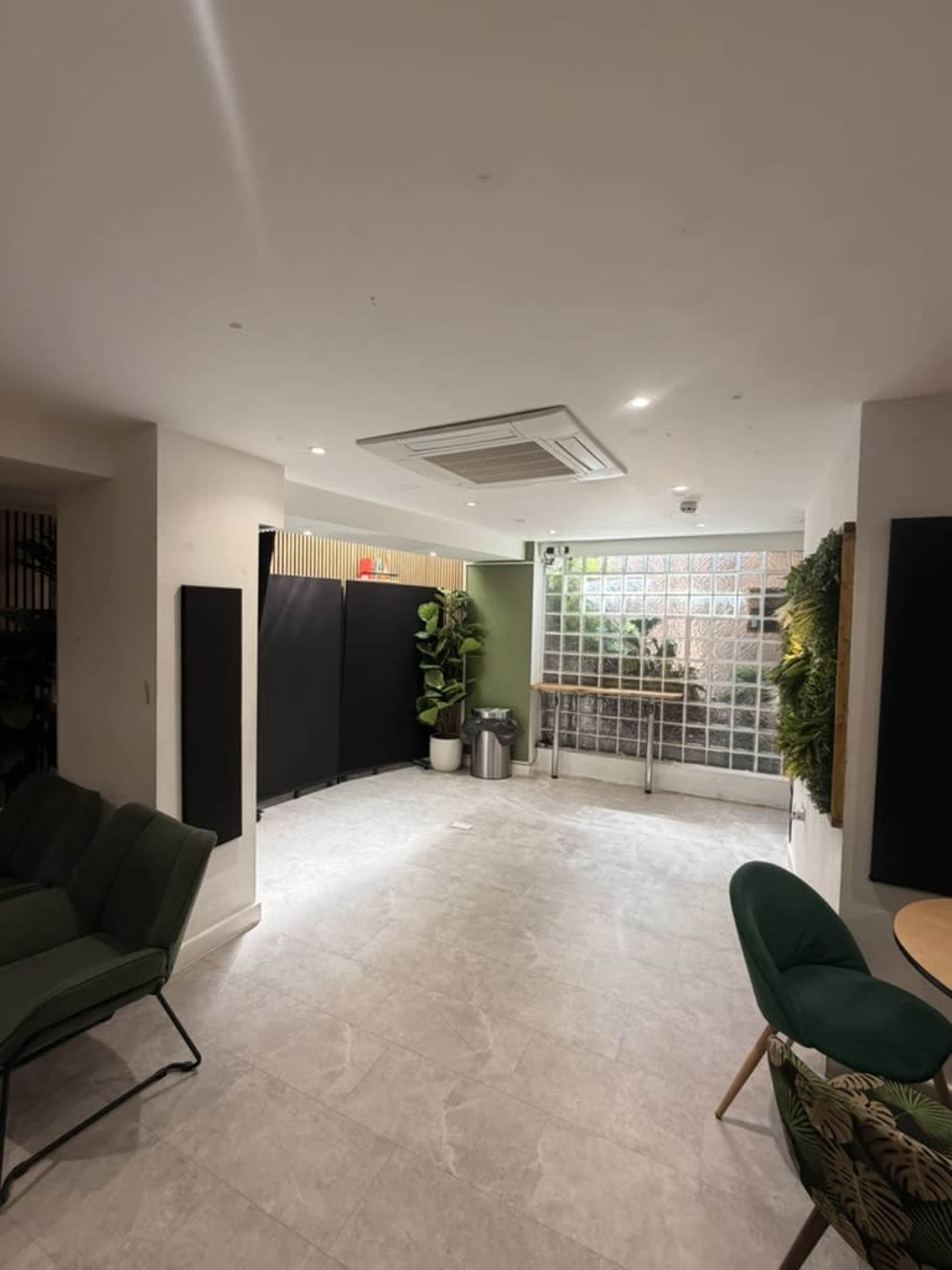 The image shows a spacious interior room with modern decor, featuring a green plant, a glass block wall, and seating arrangements.