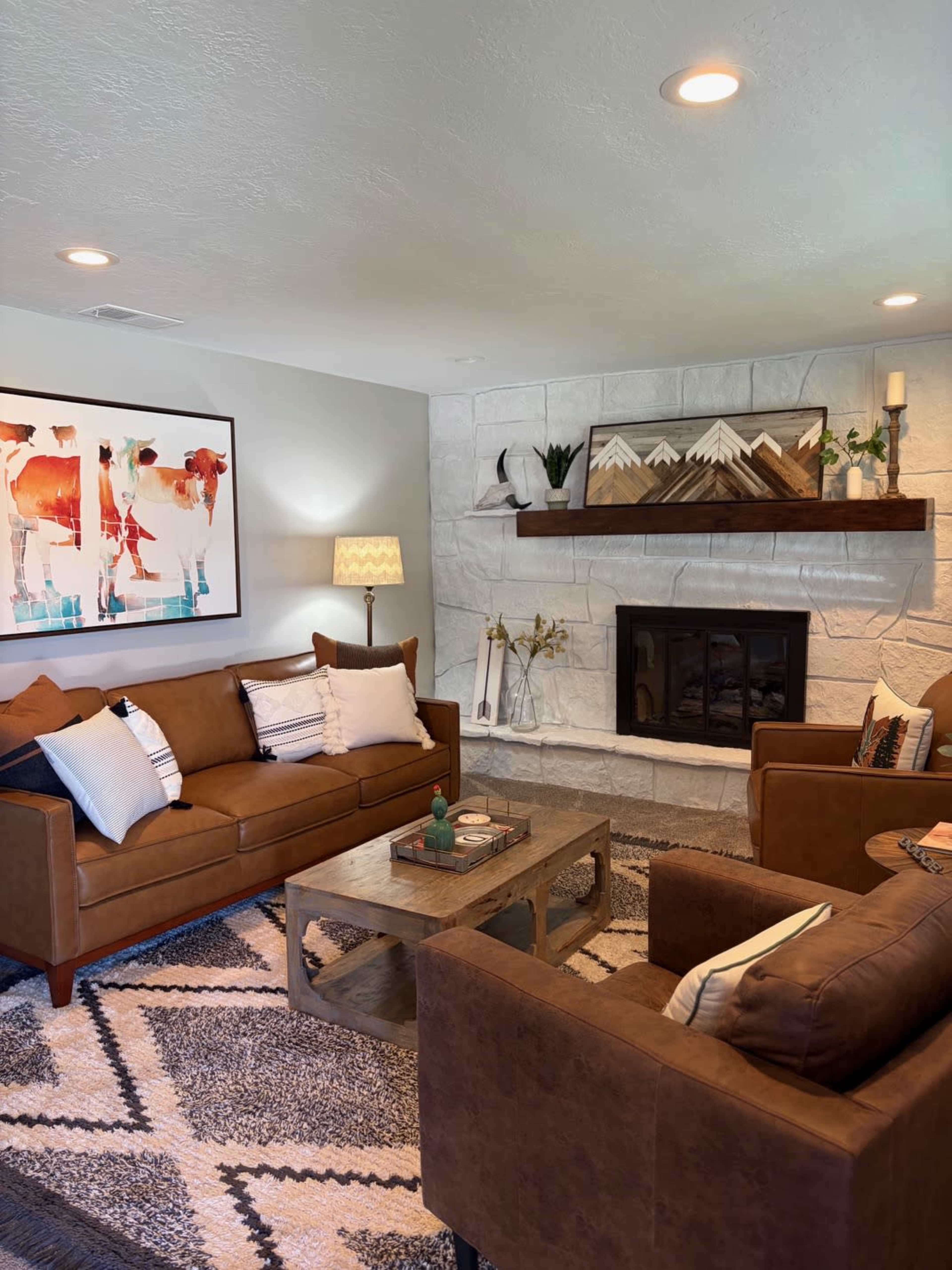 The image shows a well-furnished living room with two brown sofas, a coffee table, and a fireplace surrounded by decorative elements.