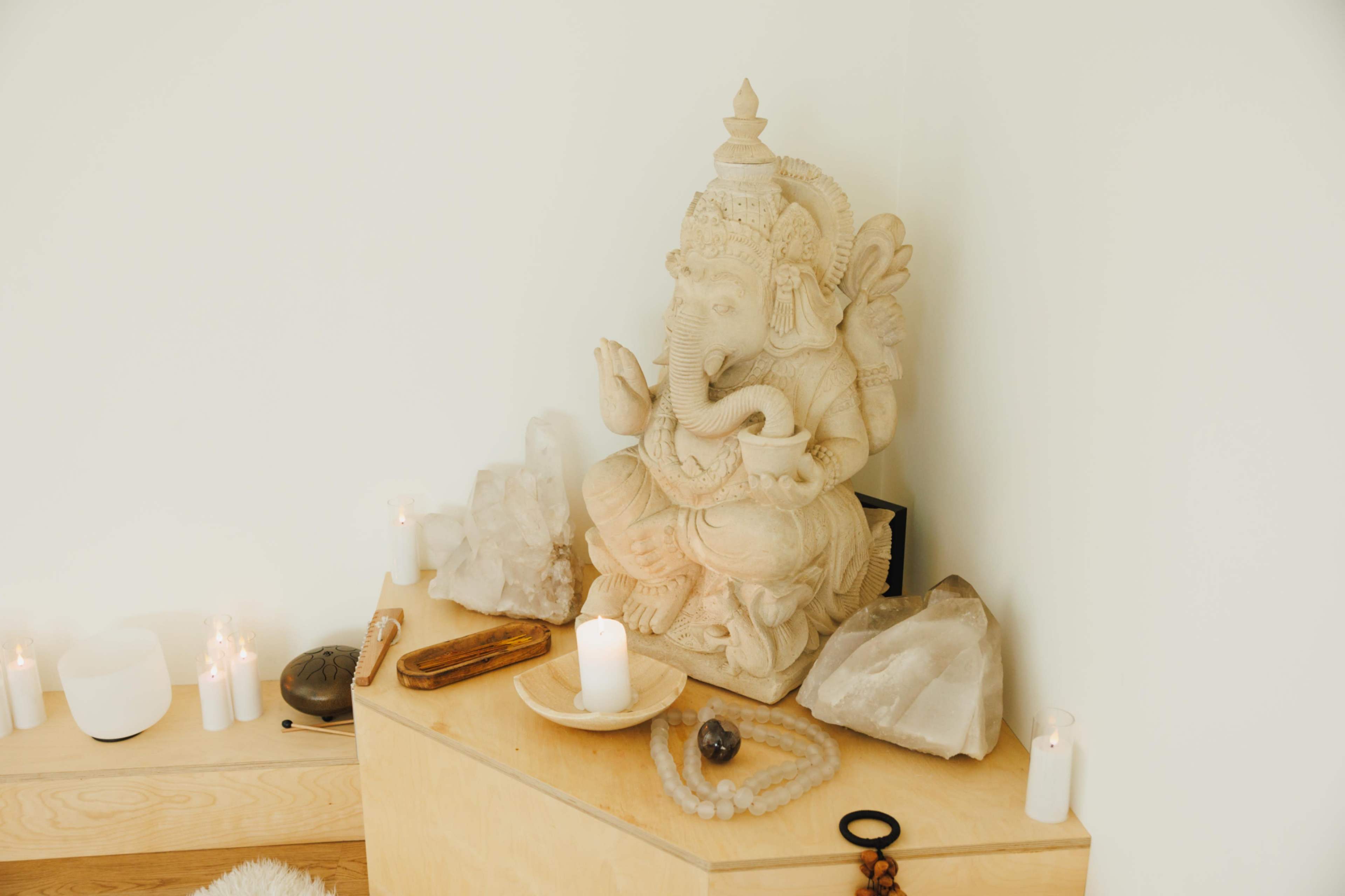 A carved stone statue of Ganesha is placed on a wooden surface, surrounded by candles, crystals, and decorative items.