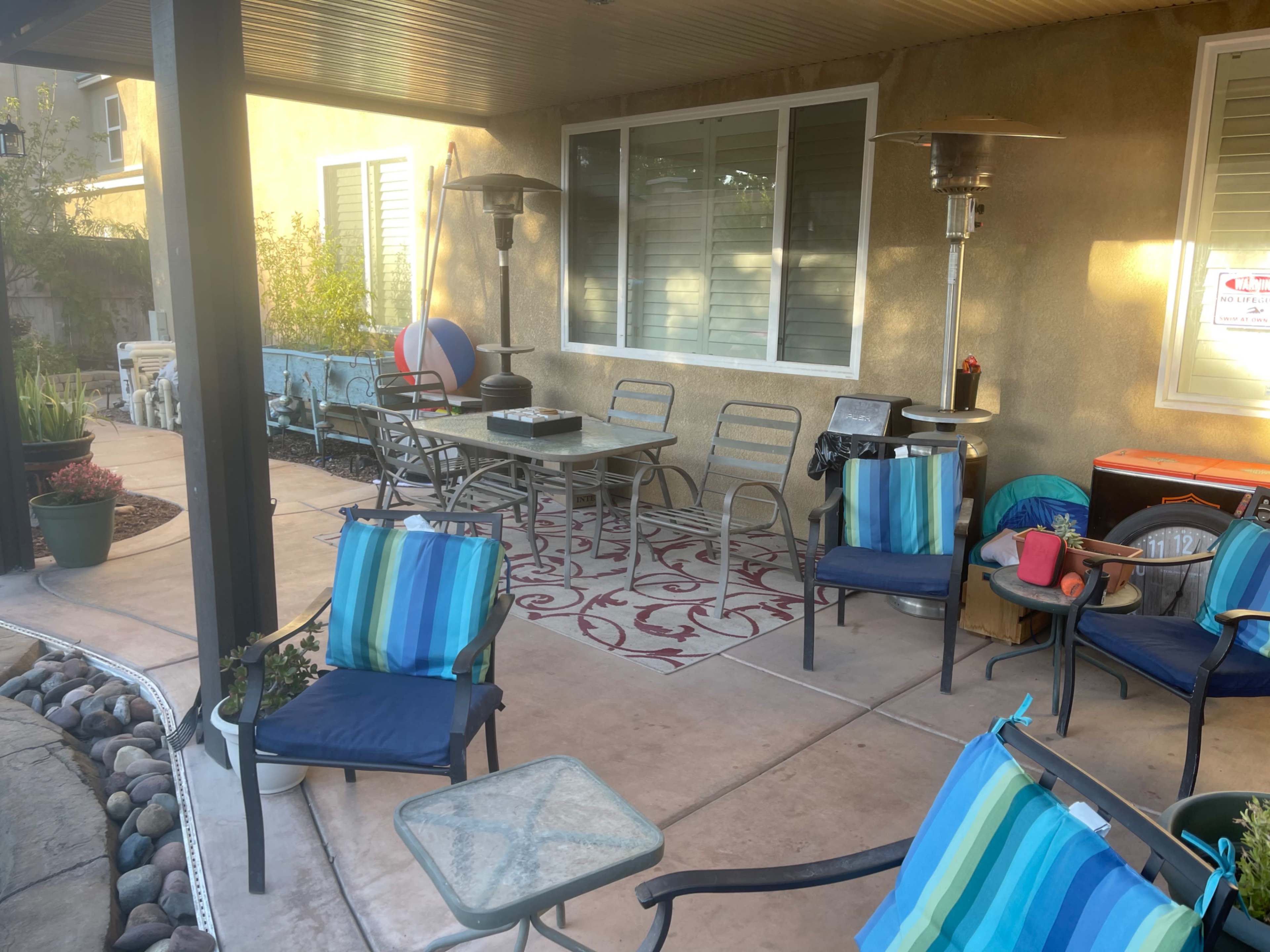 A patio area features several blue-striped chairs and a table, along with a heater, decorative items, and a large beach ball.