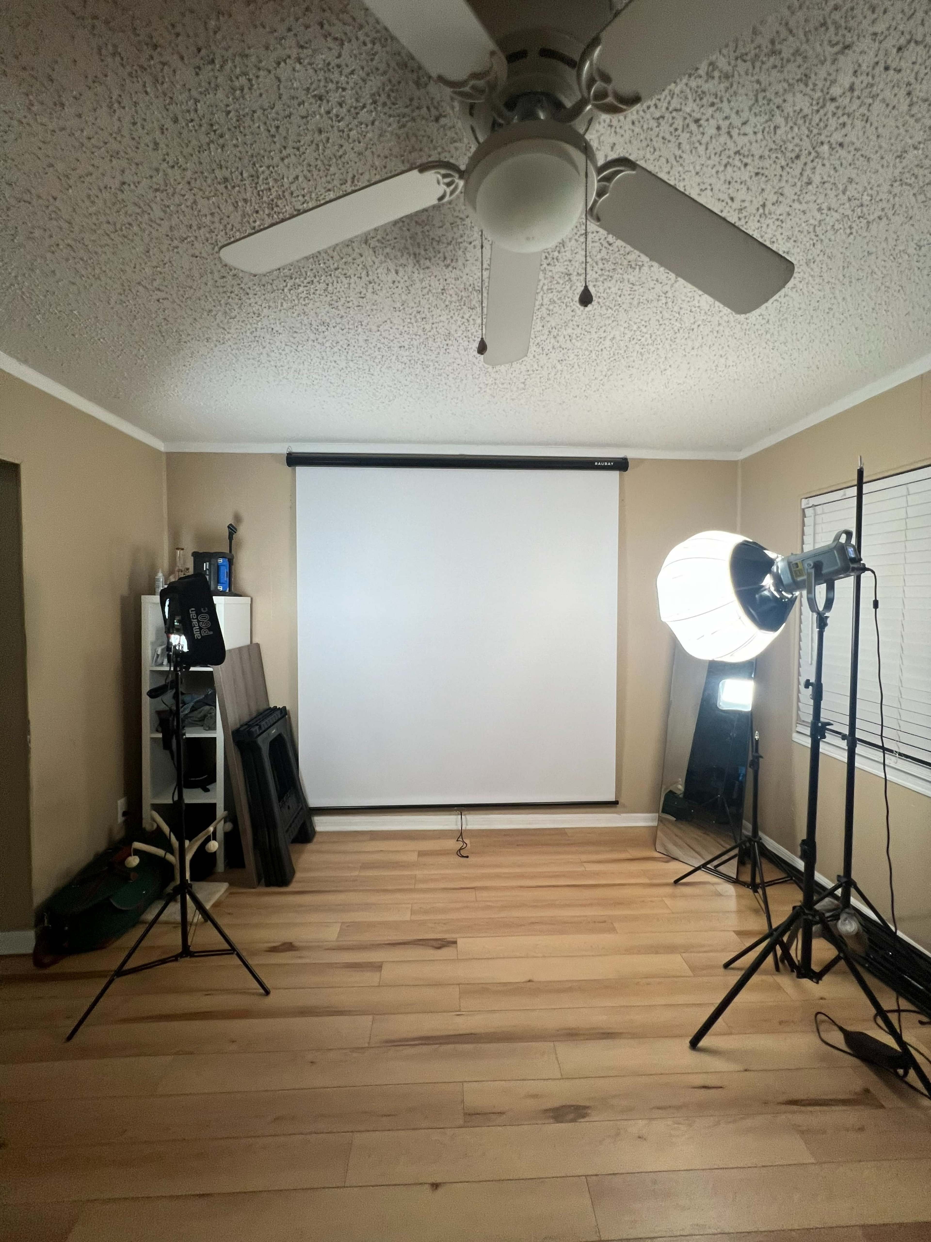 A well-lit room with a ceiling fan, a retractable projection screen, and two lighting setups on stands.