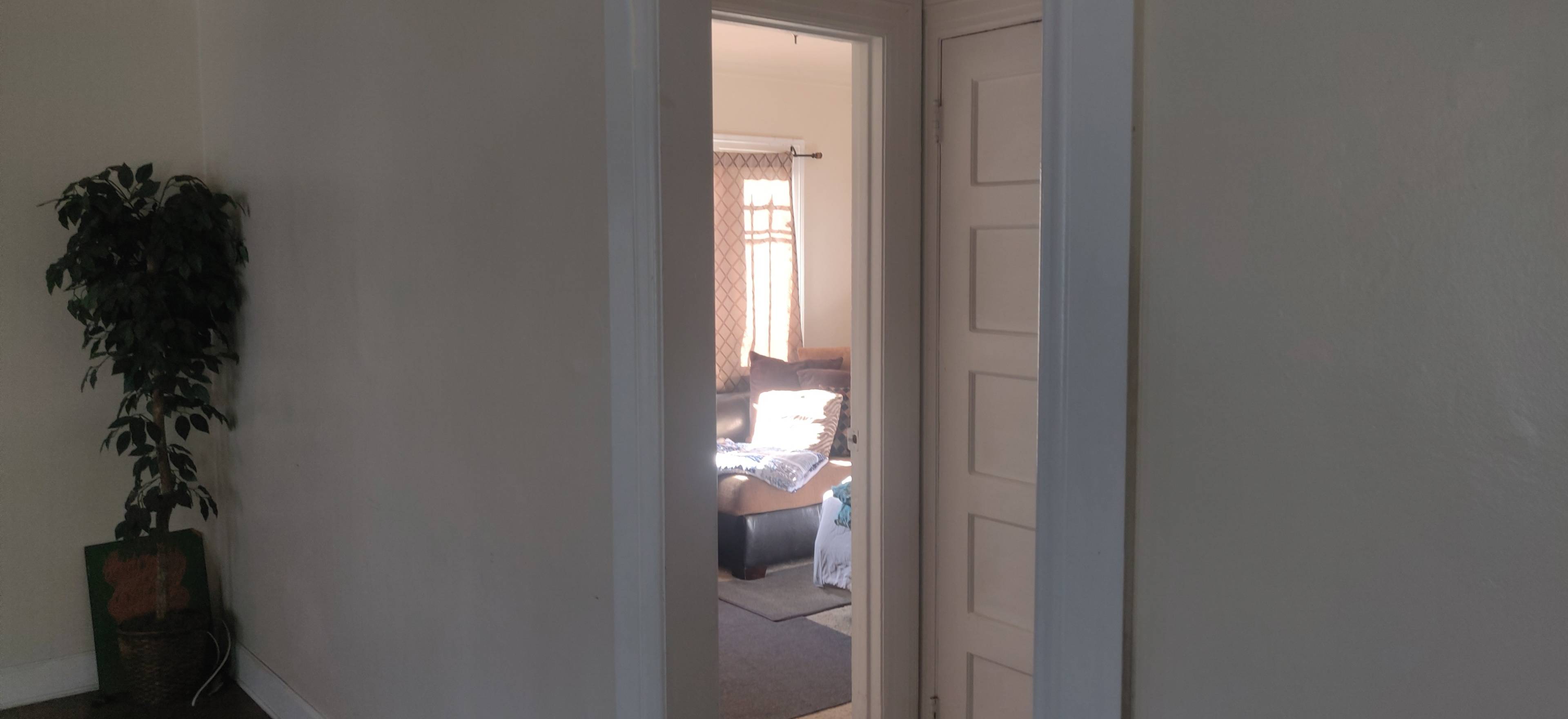A doorway leads to a room with a couch and a window partially covered by curtains.