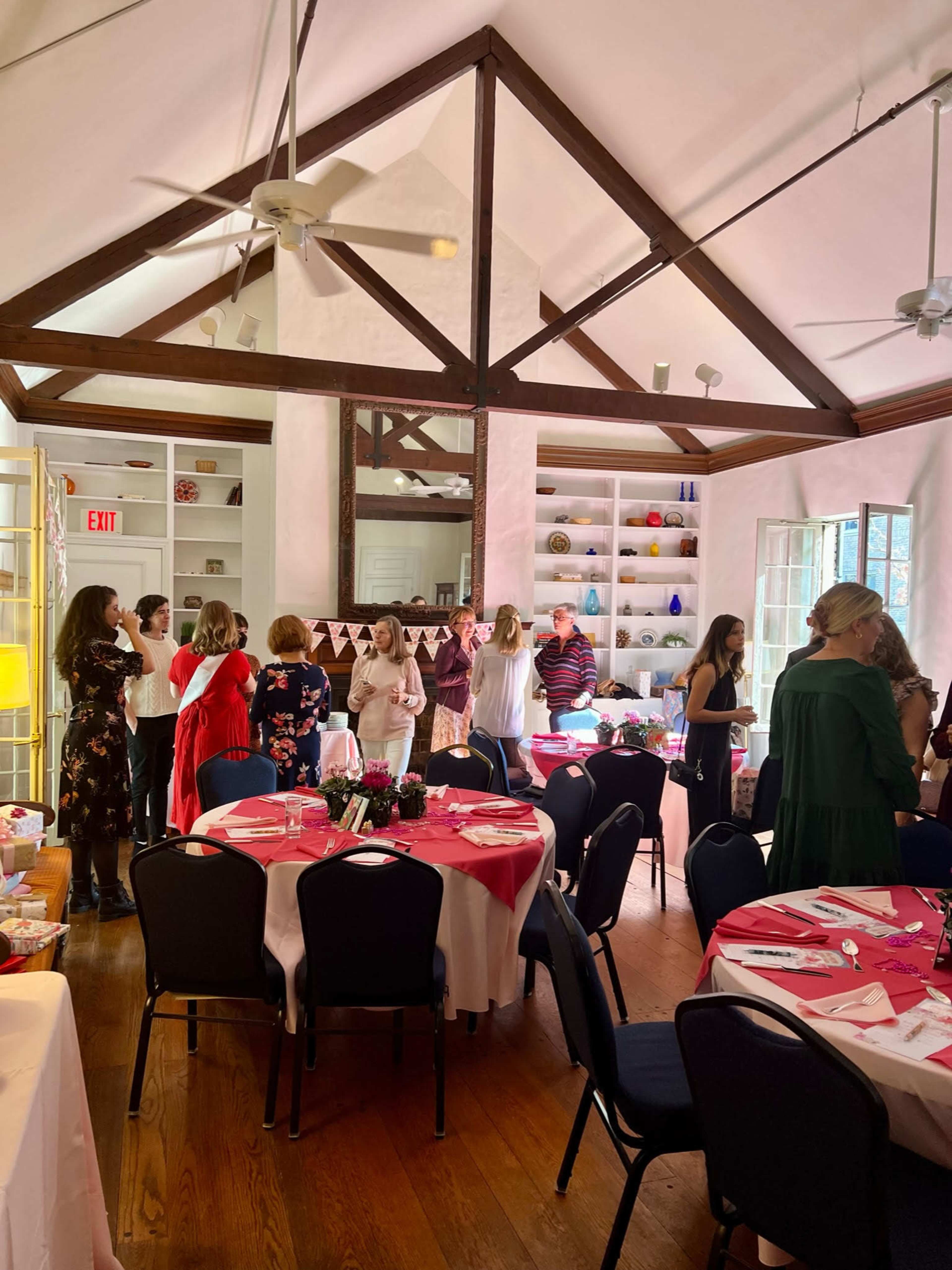 A group of people are gathered in a room decorated for a celebration, with tables set for dining and a display of colorful decorations on the shelves.