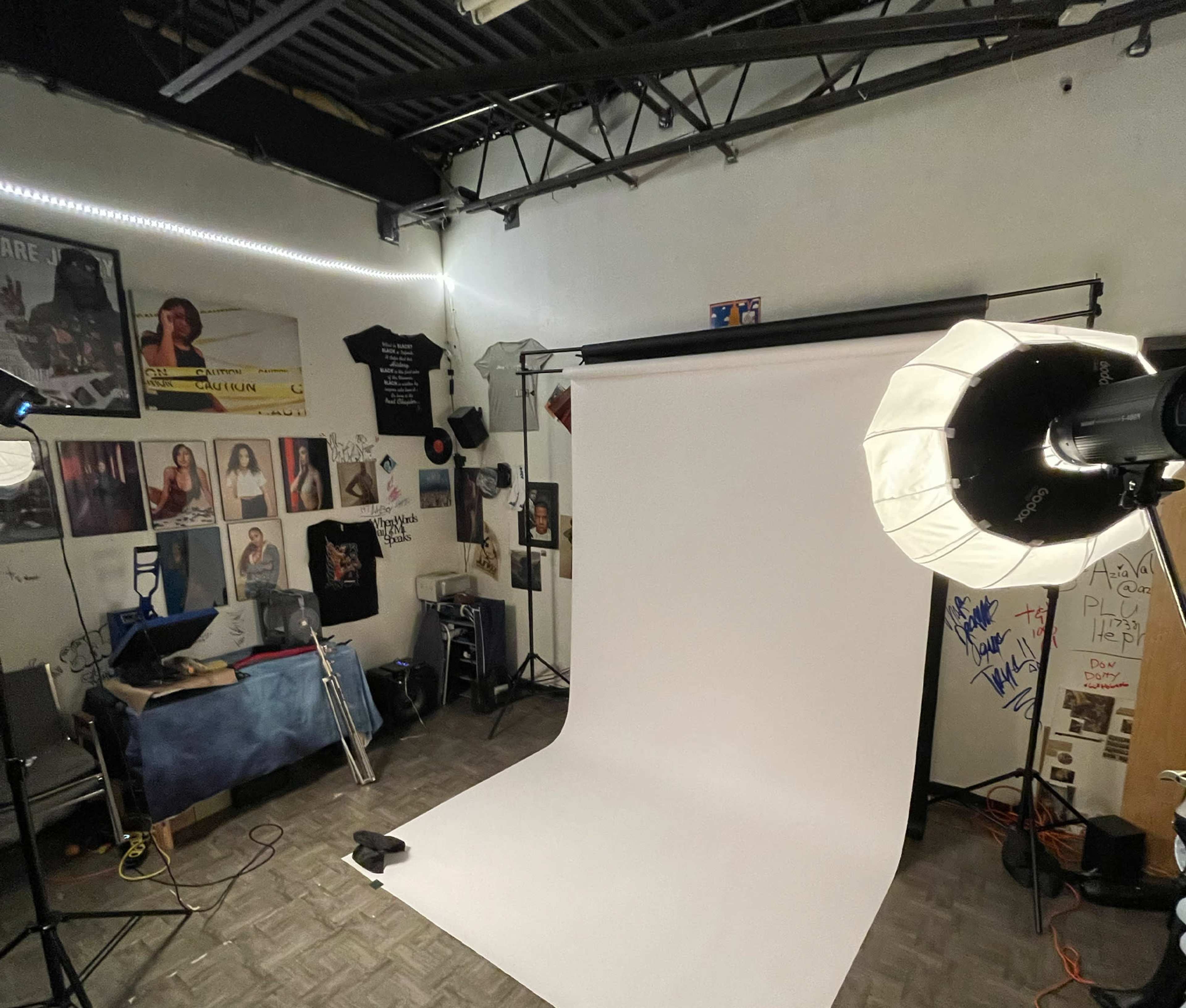 A photography studio featuring a white backdrop, lighting equipment, and various framed photographs on the walls.