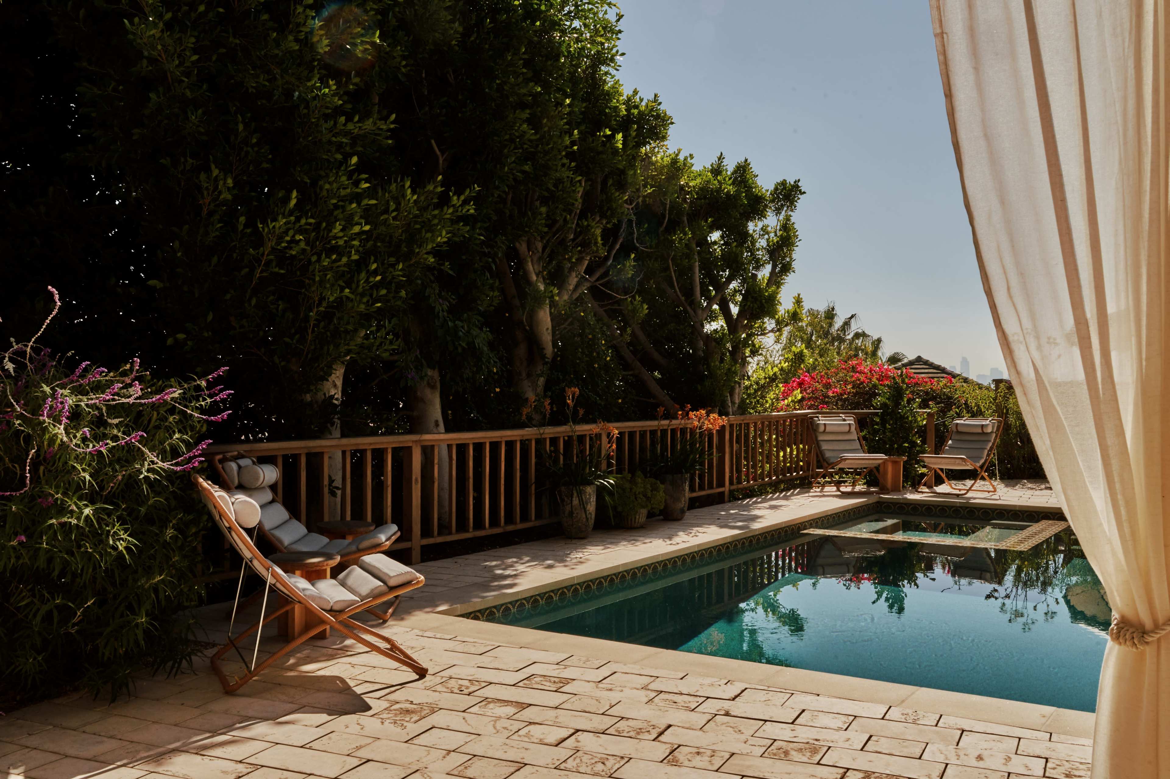 A serene outdoor space features a swimming pool surrounded by lush greenery, with two lounge chairs nearby.