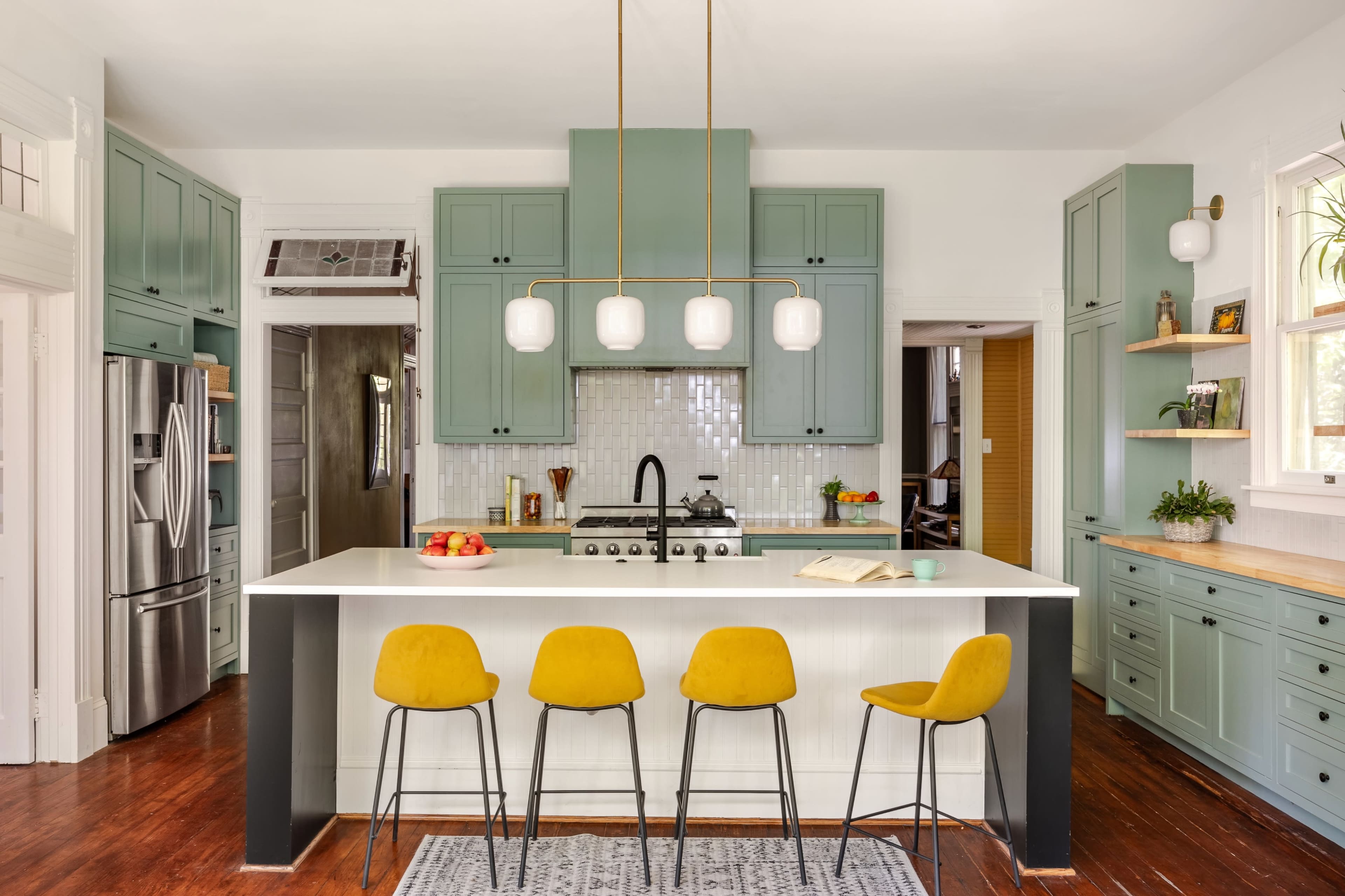 The image shows a modern kitchen with teal cabinets, a white island with bar stools, and pendant lighting above the countertop.