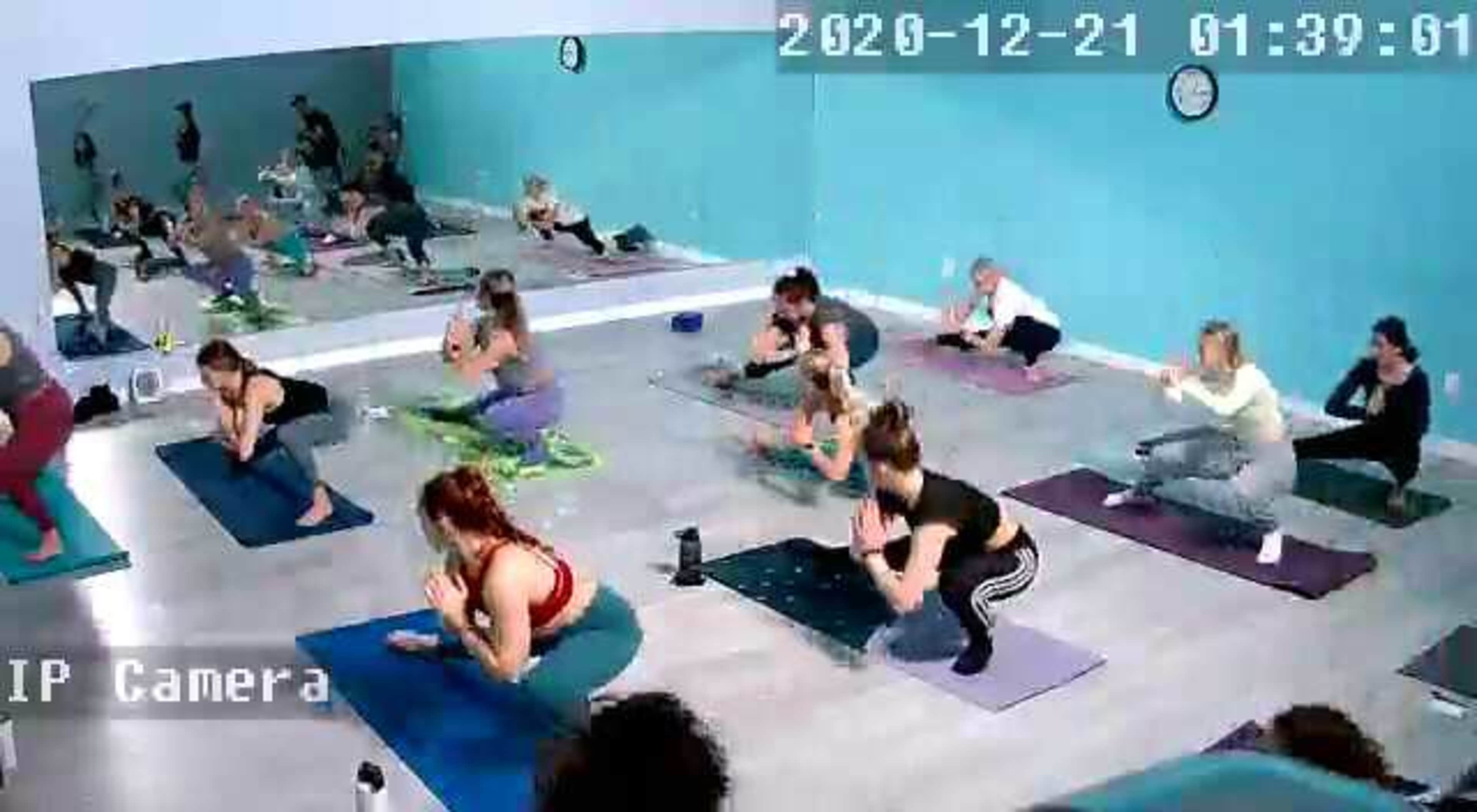 A group of people is practicing yoga in a studio with large mirrors and a light blue wall.