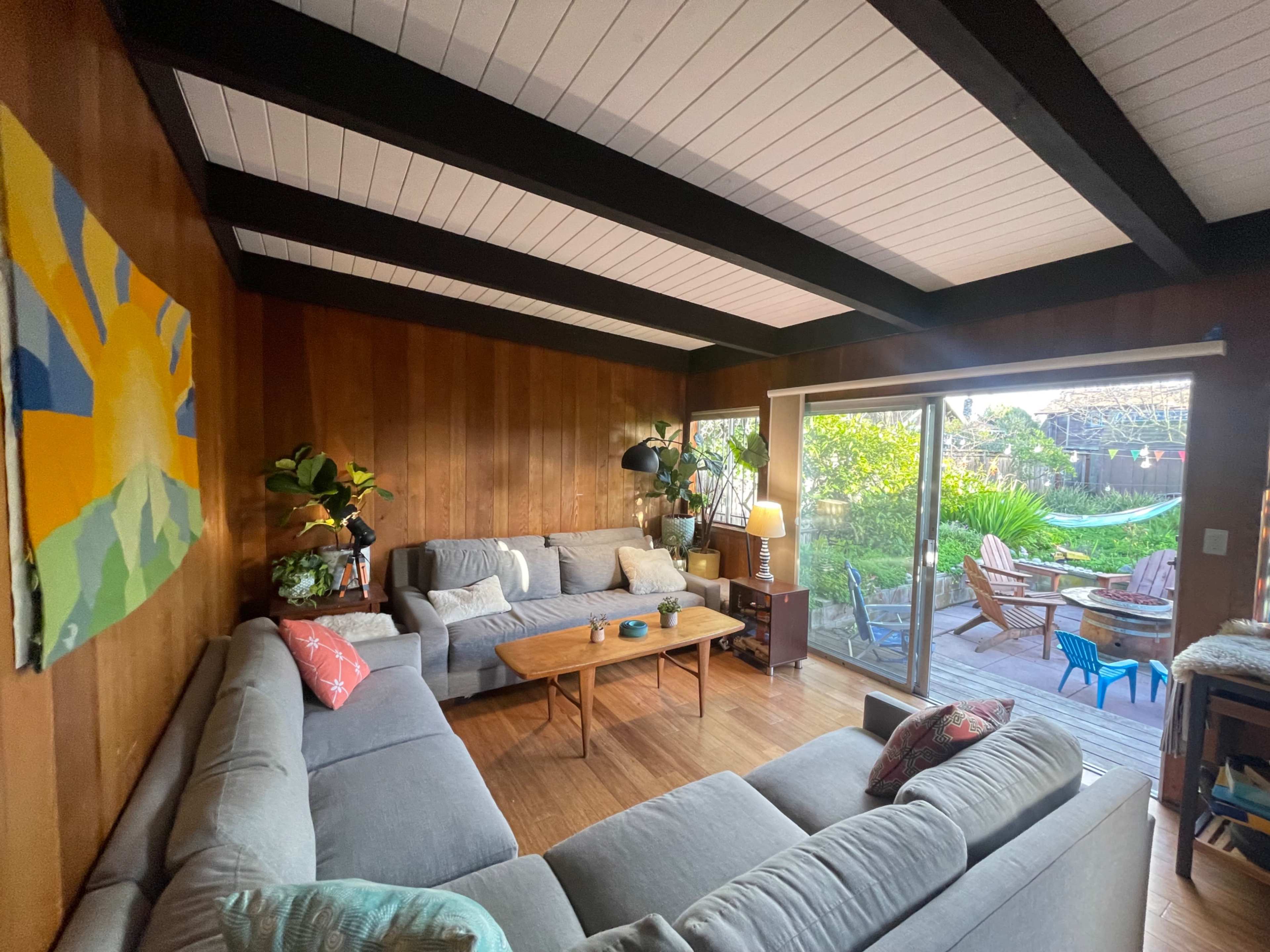 A modern living room features a sectional sofa arranged around a wooden coffee table, with large sliding glass doors opening to a backyard garden.