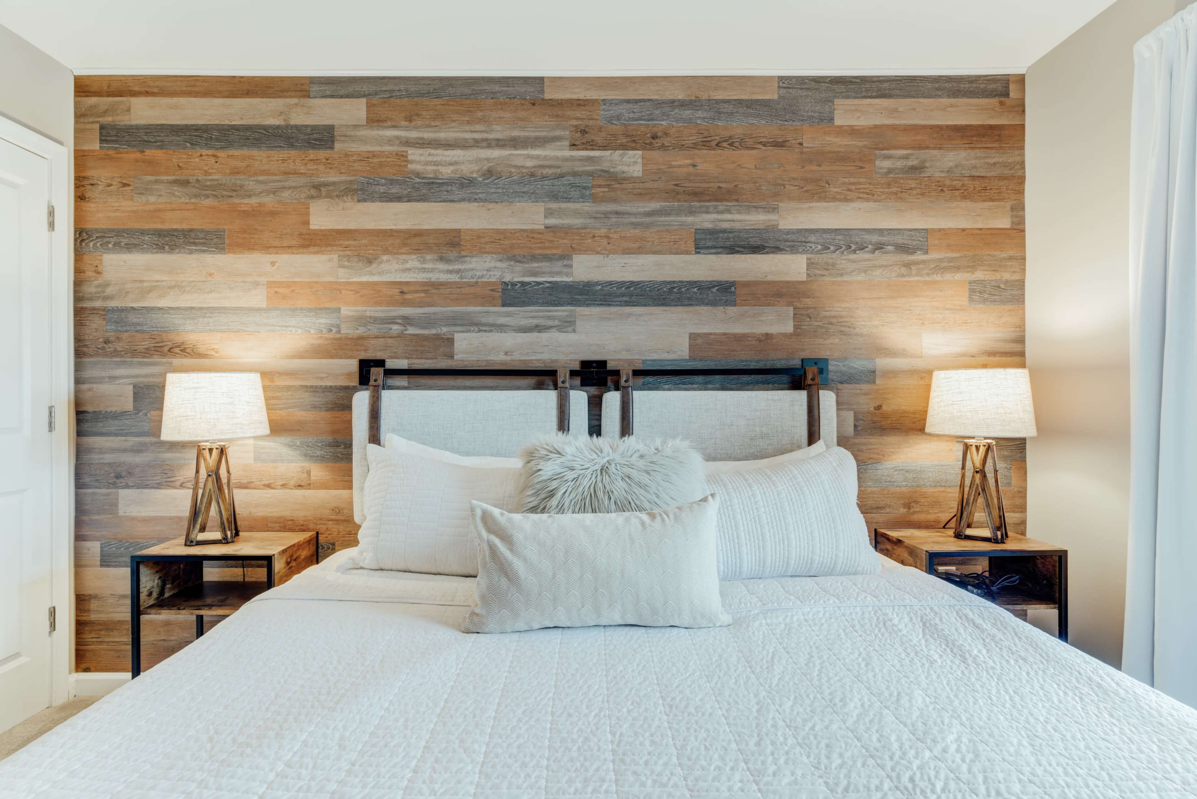 A neatly made bed with a white quilt, flanked by two bedside tables with lamps, set against a wooden accent wall.