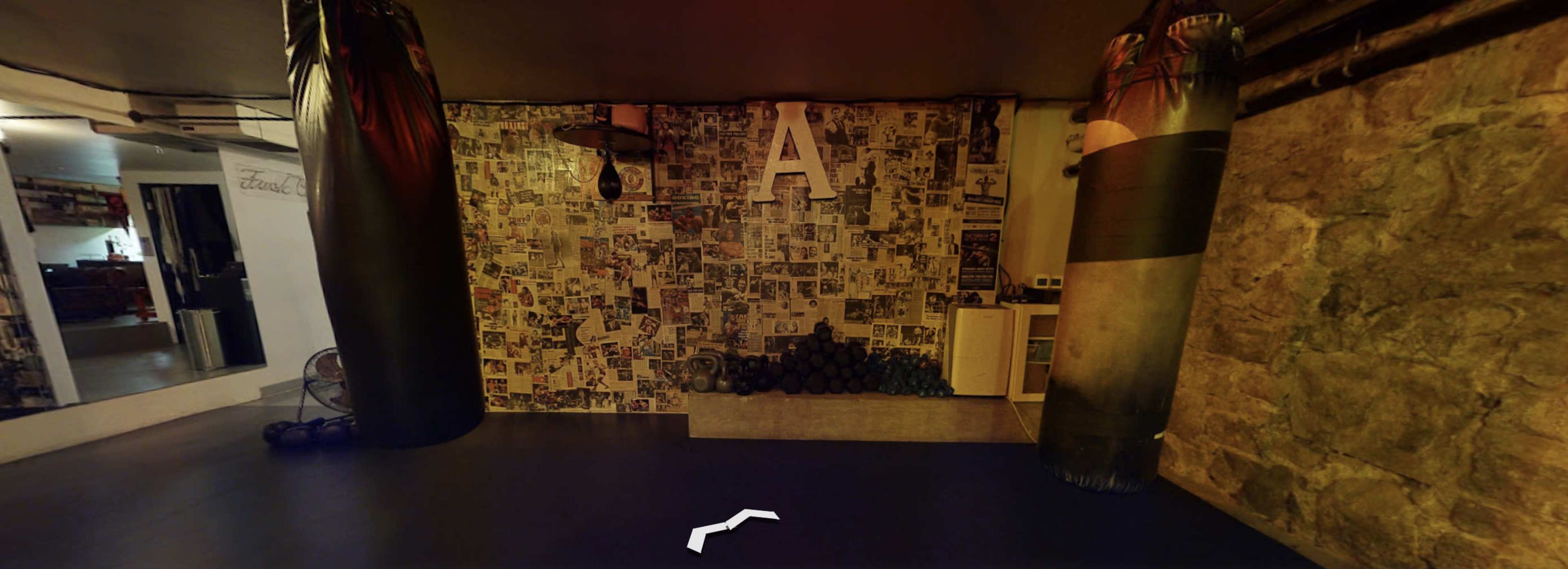 A gym space with two punching bags, a wall covered in black-and-white photos, and a row of dumbbells in the corner.