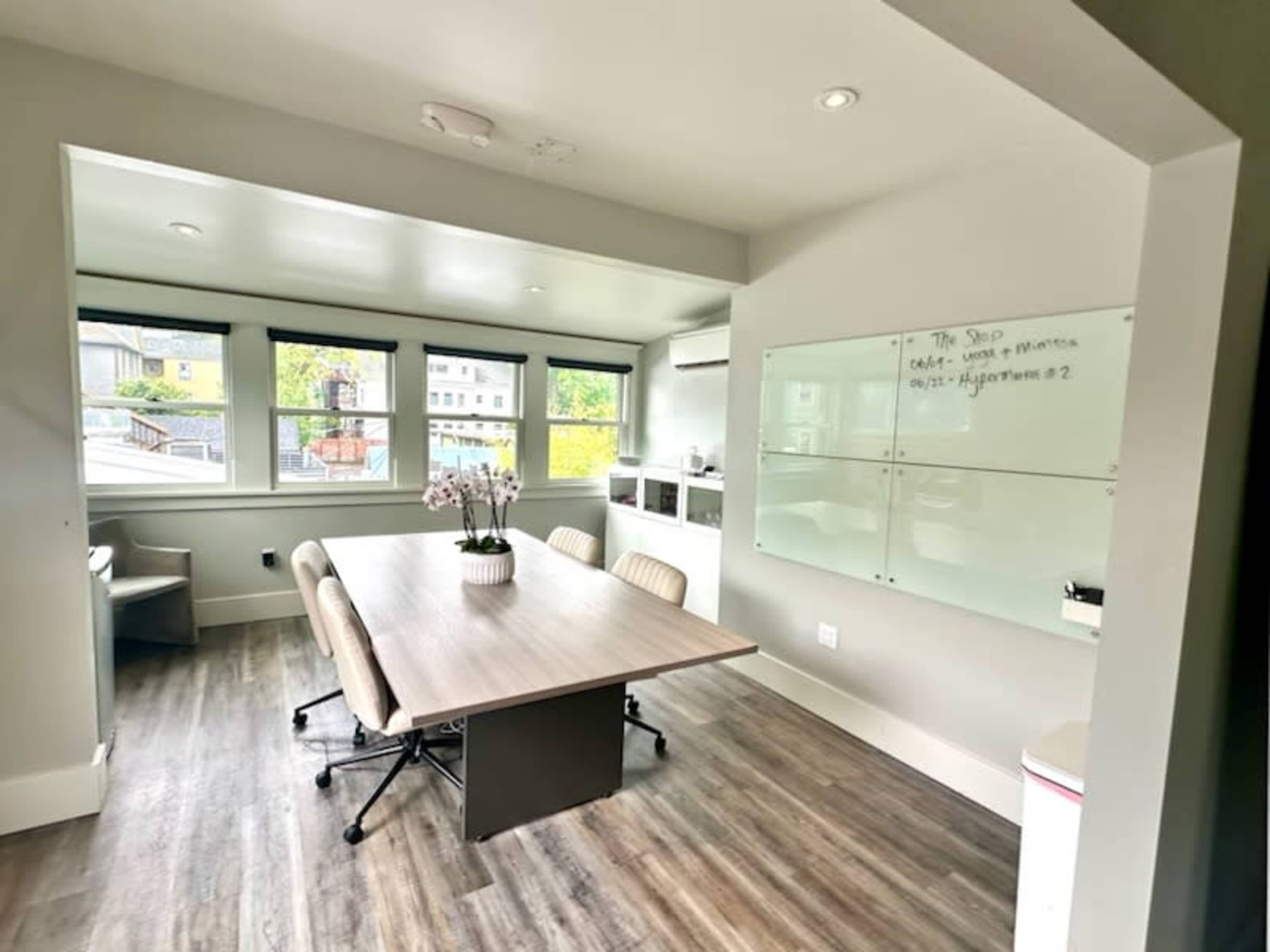 A modern office space with a large table, chairs, and whiteboards in a well-lit room featuring several windows.