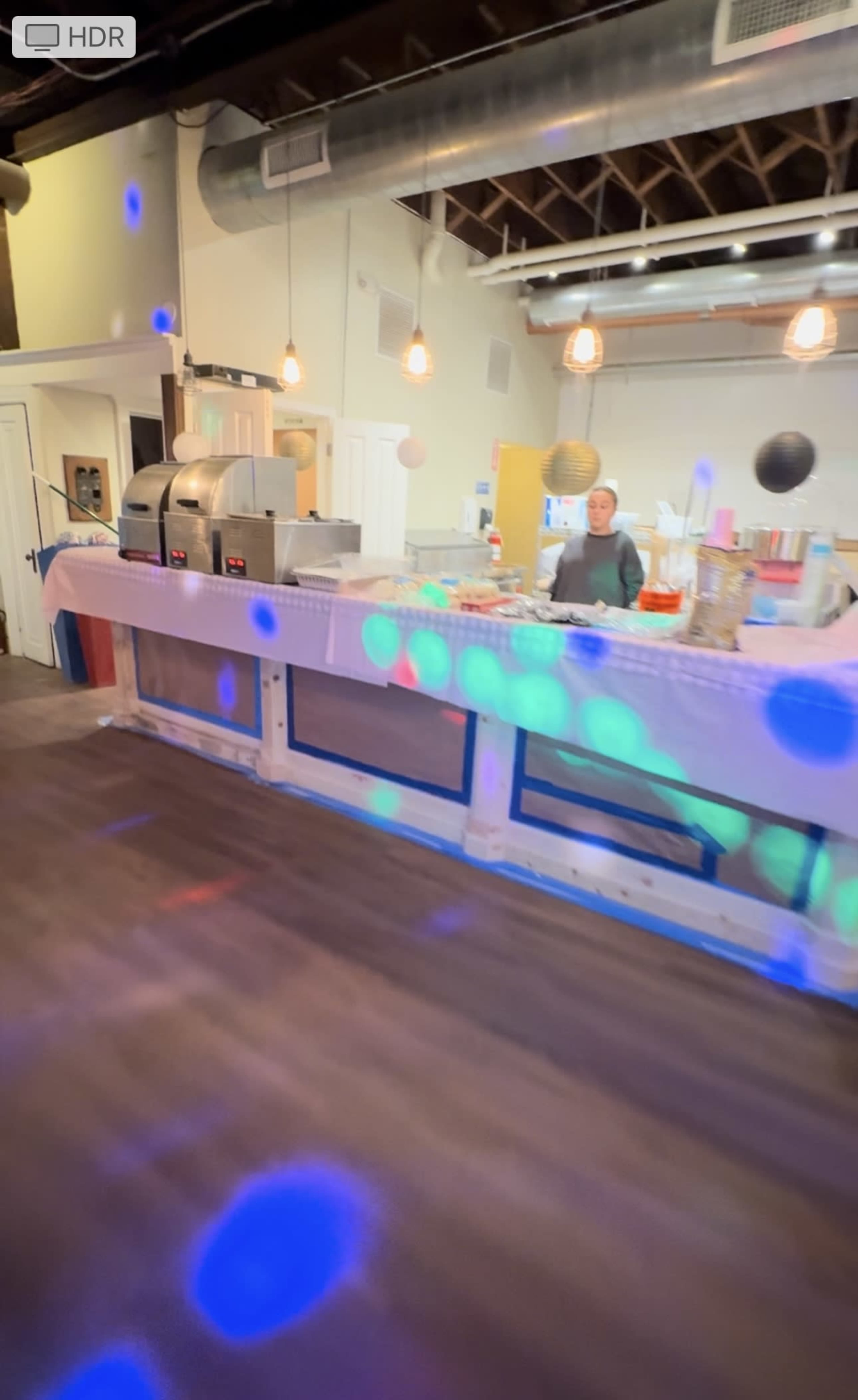 The image shows a brightly lit kitchen area with a countertop, appliances, and a person standing behind the counter.