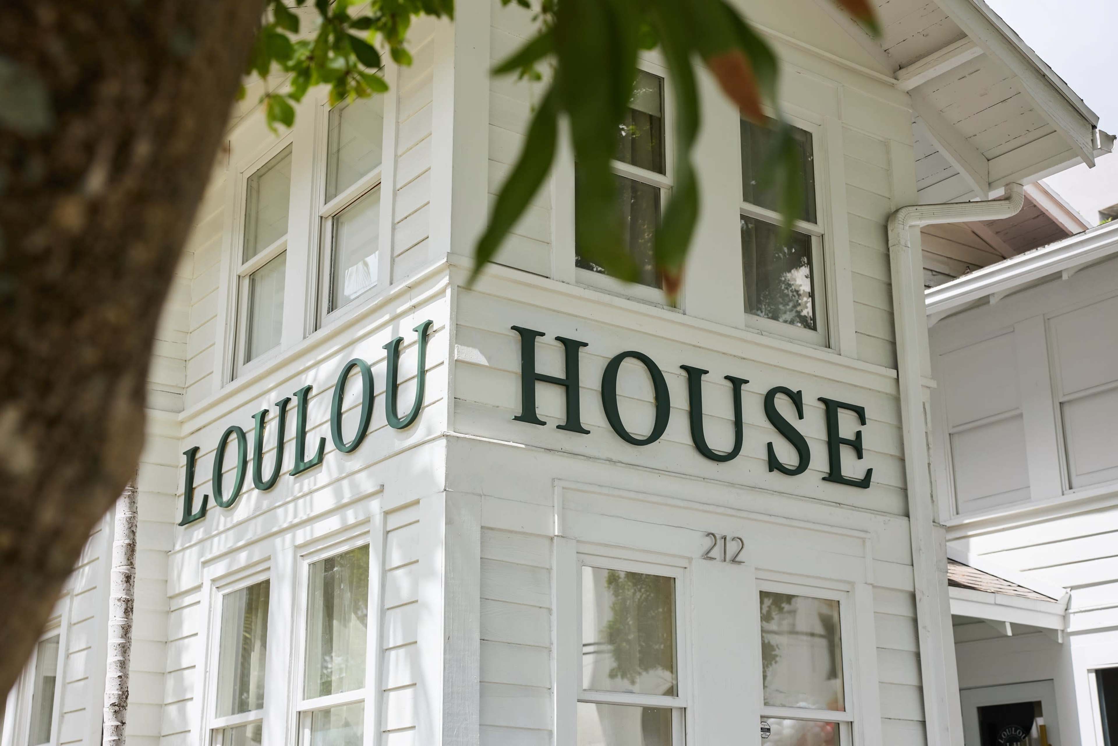 The image shows a white building with the words "LOULOU HOUSE" prominently displayed on its exterior.