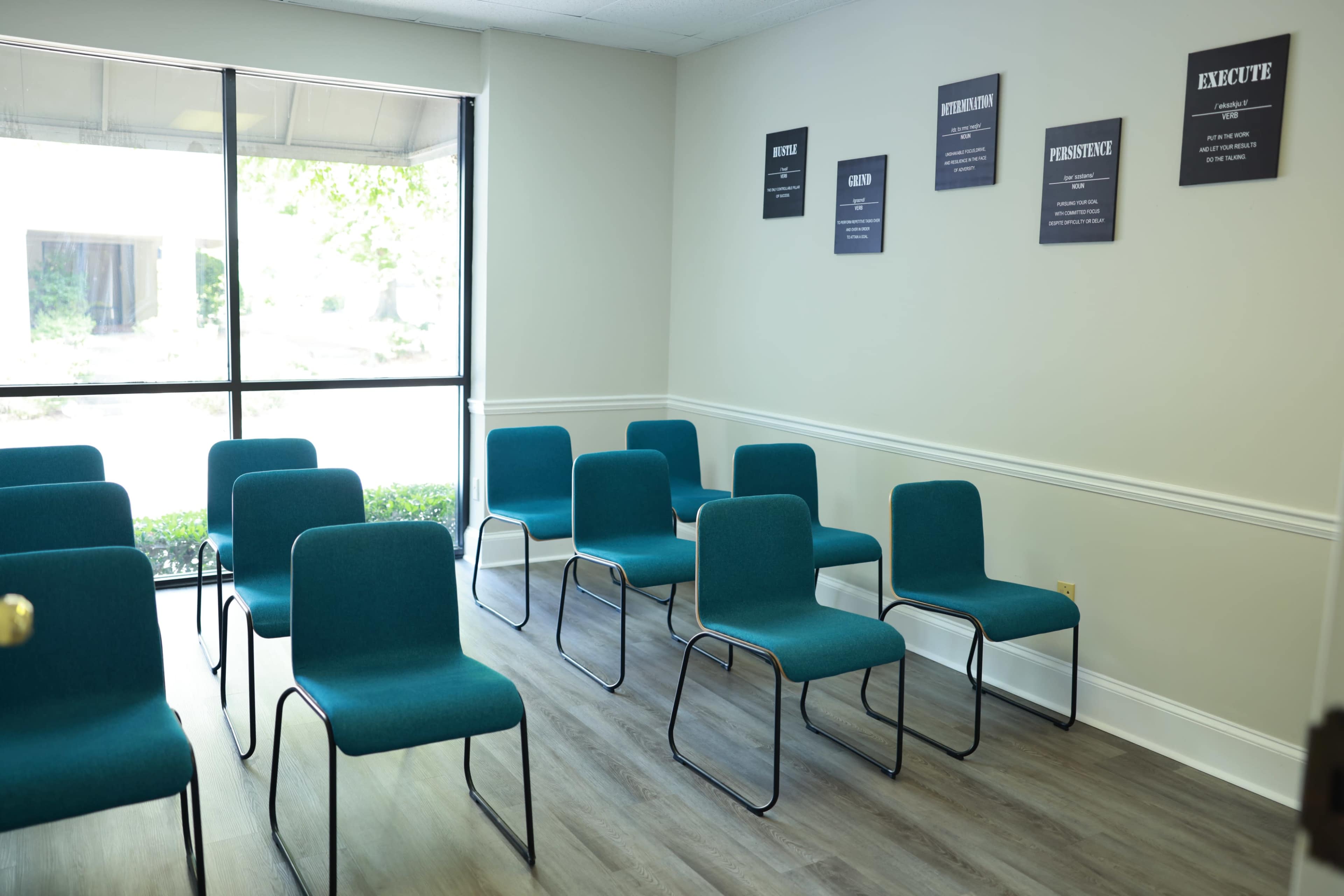 A room with several teal chairs arranged in rows facing a window, with motivational posters on the wall.
