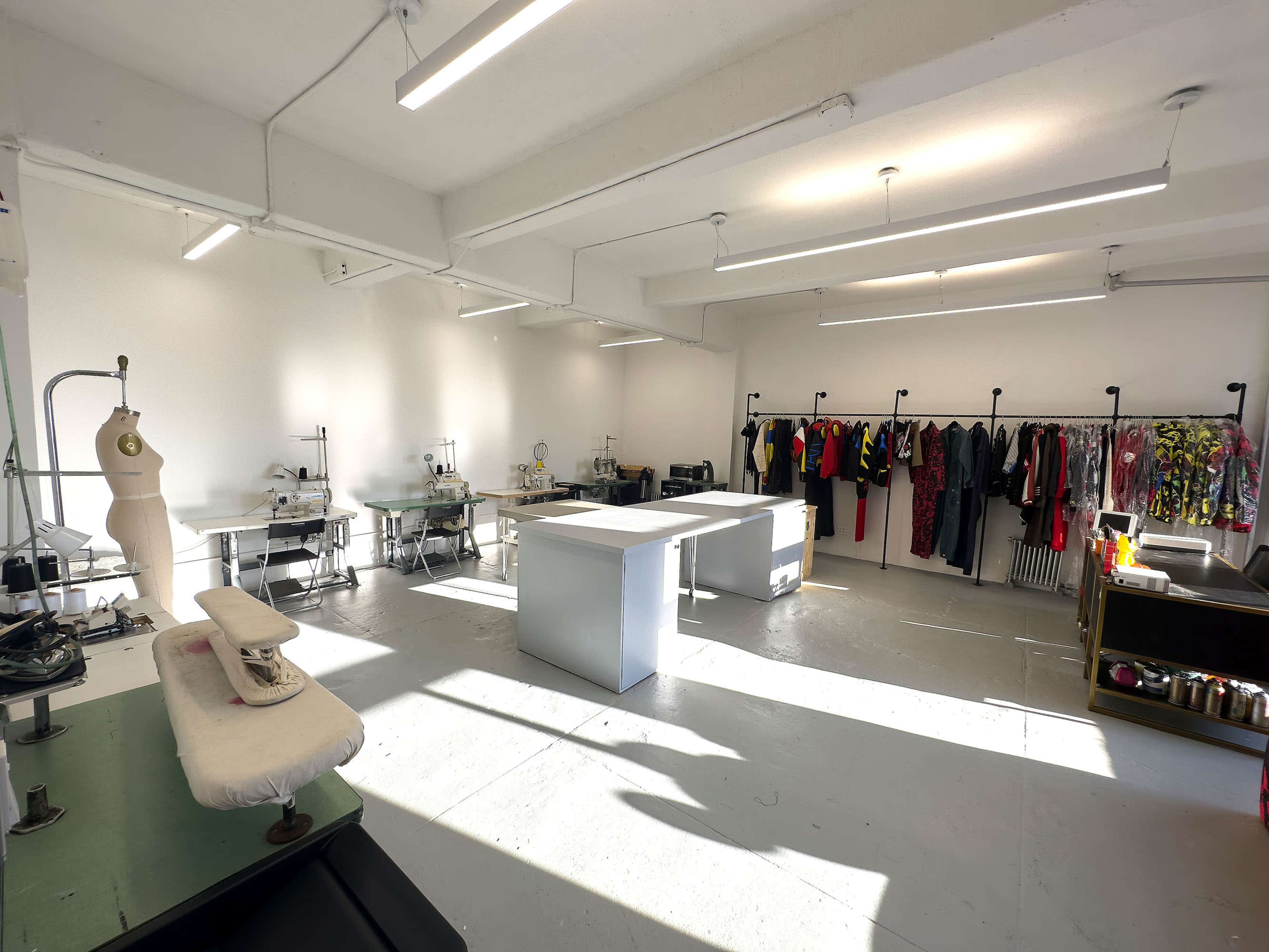 A spacious design studio with sewing equipment and clothing displayed on racks along the walls.