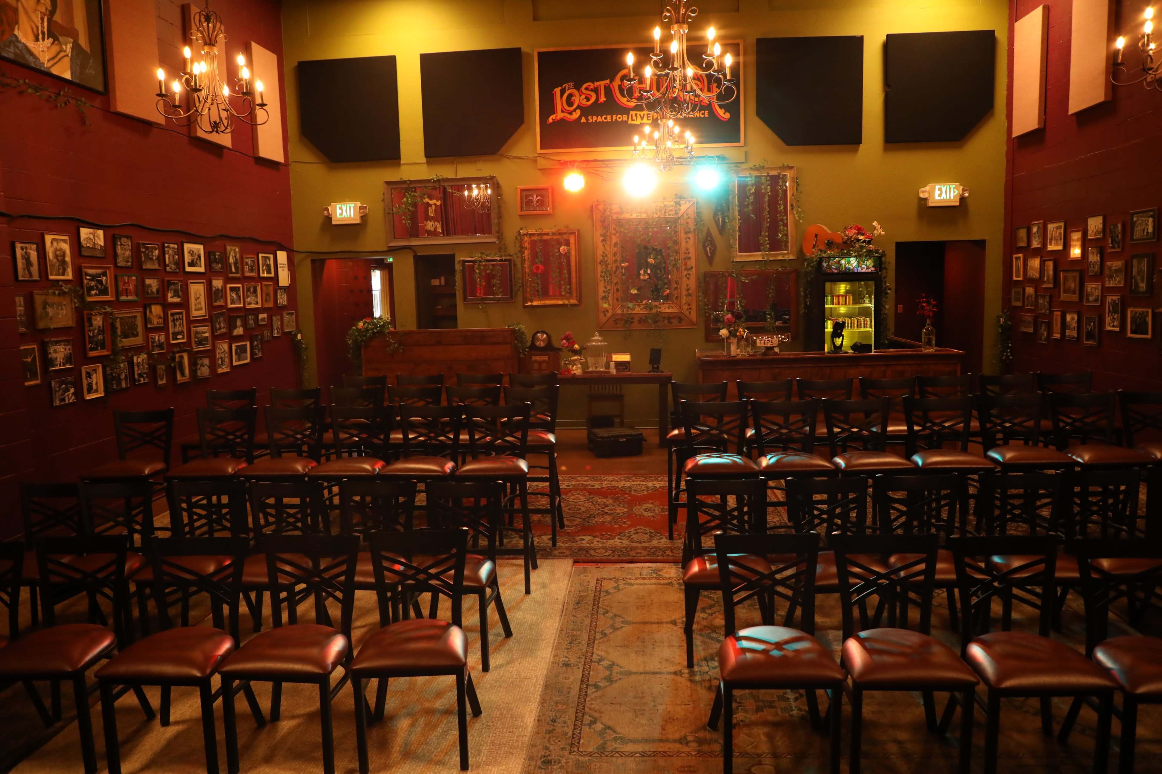 The image shows an empty performance venue with rows of chairs arranged facing a small stage adorned with decorative artwork and lighting.