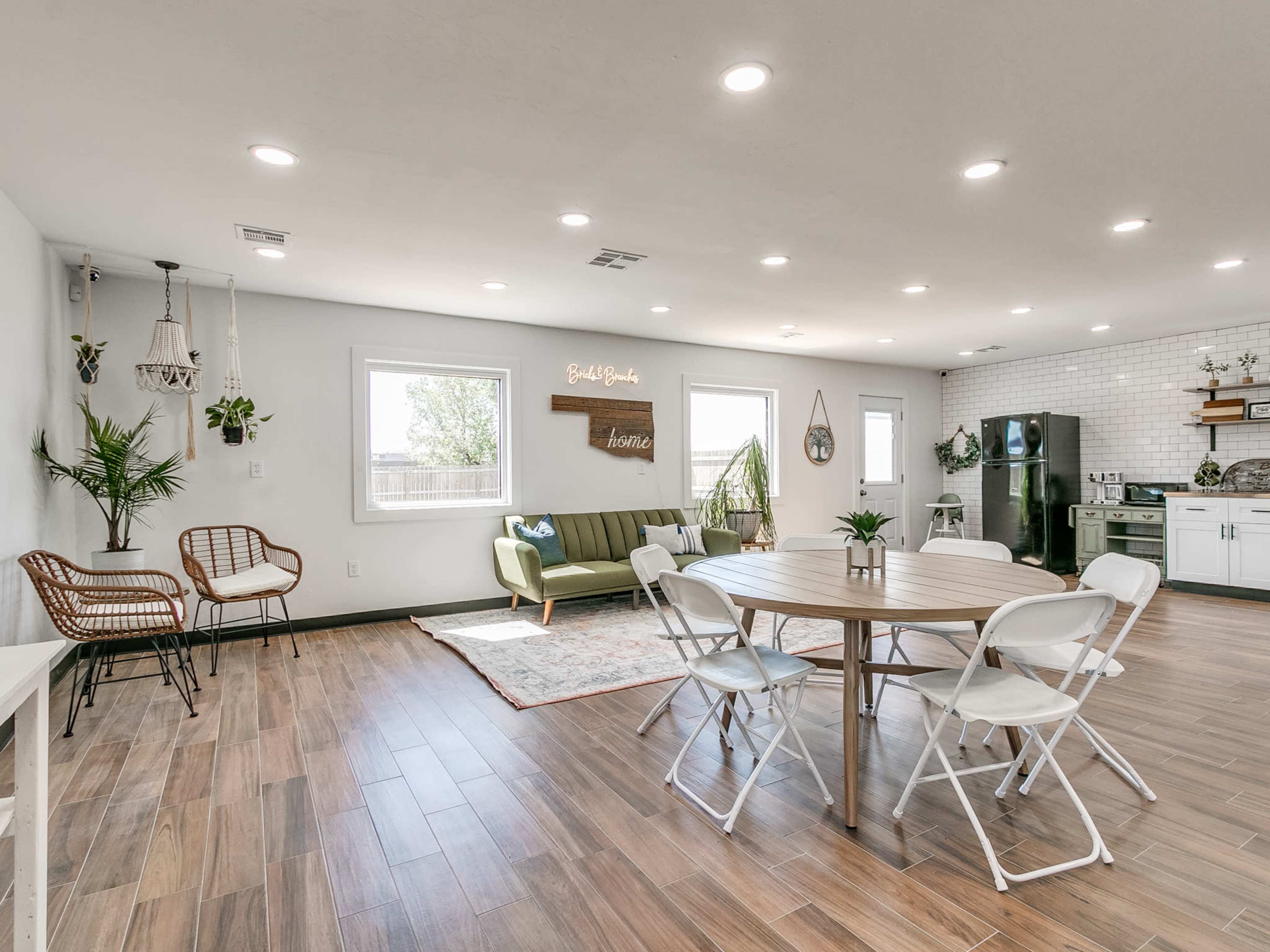 A modern living area features a green sofa, a round table with white chairs, and natural light coming through large windows.