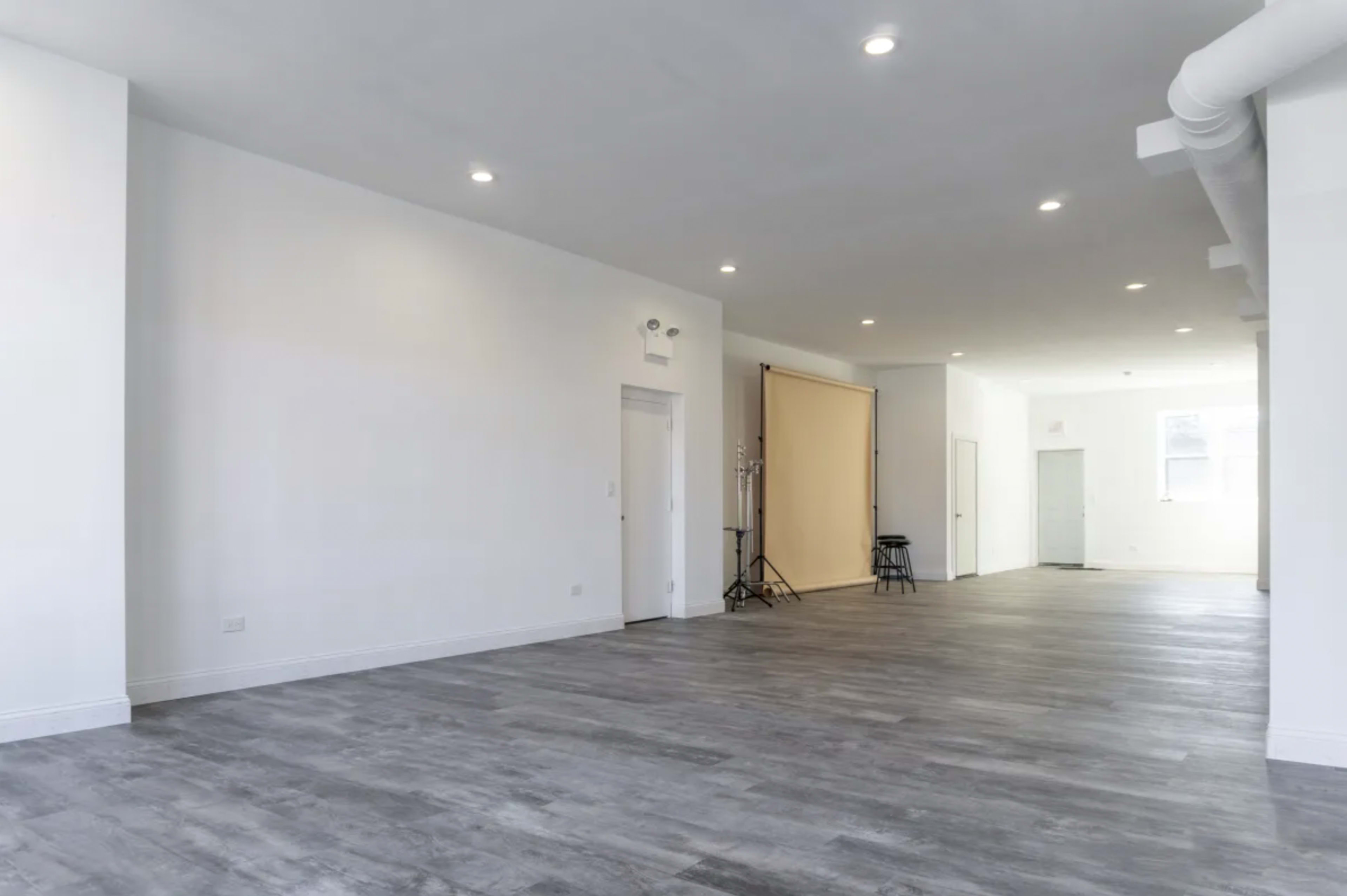 A spacious, empty room with wood-like flooring and bright overhead lights.