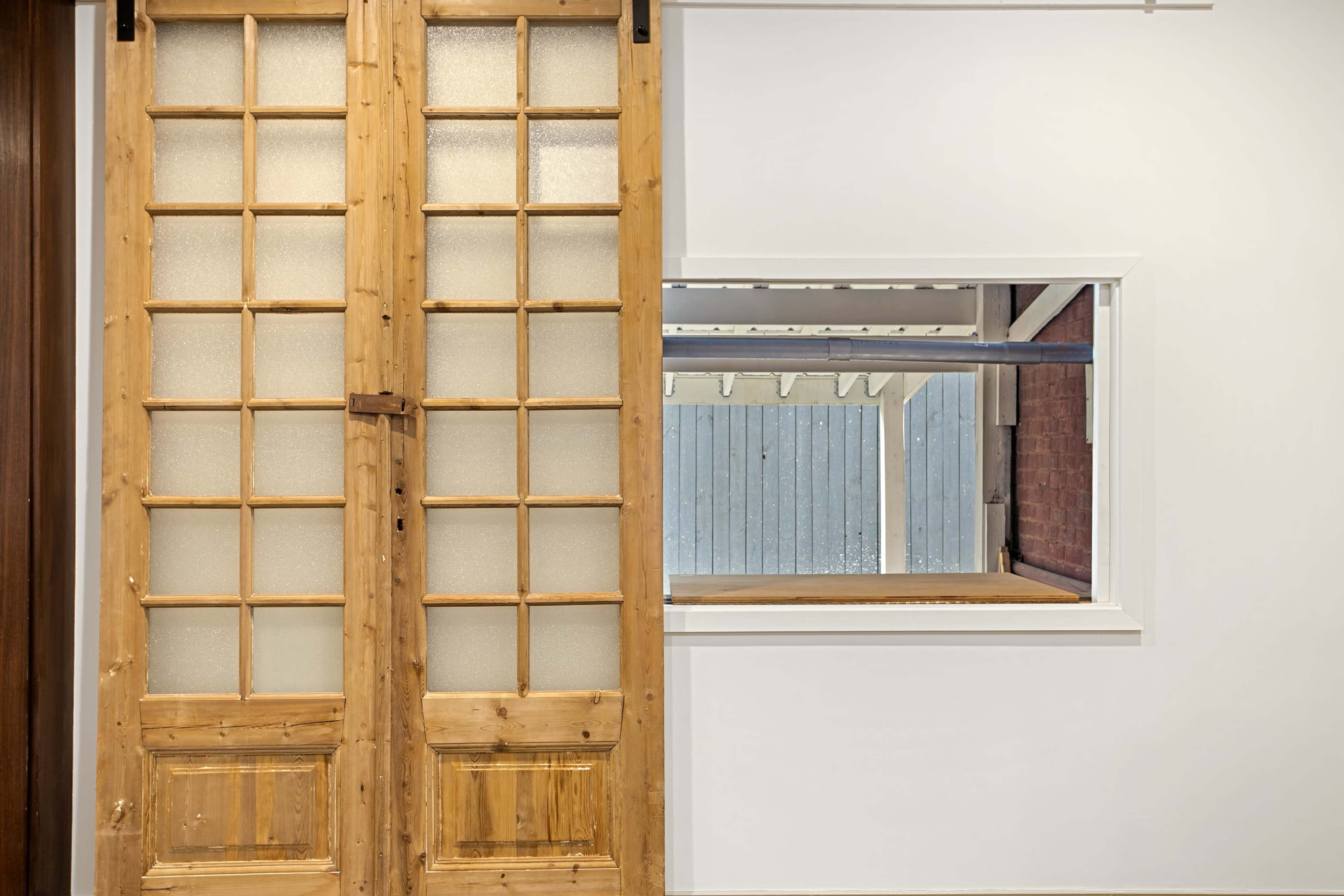 A wooden sliding door with glass panes next to a rectangular opening that overlooks a brick and wood interior.