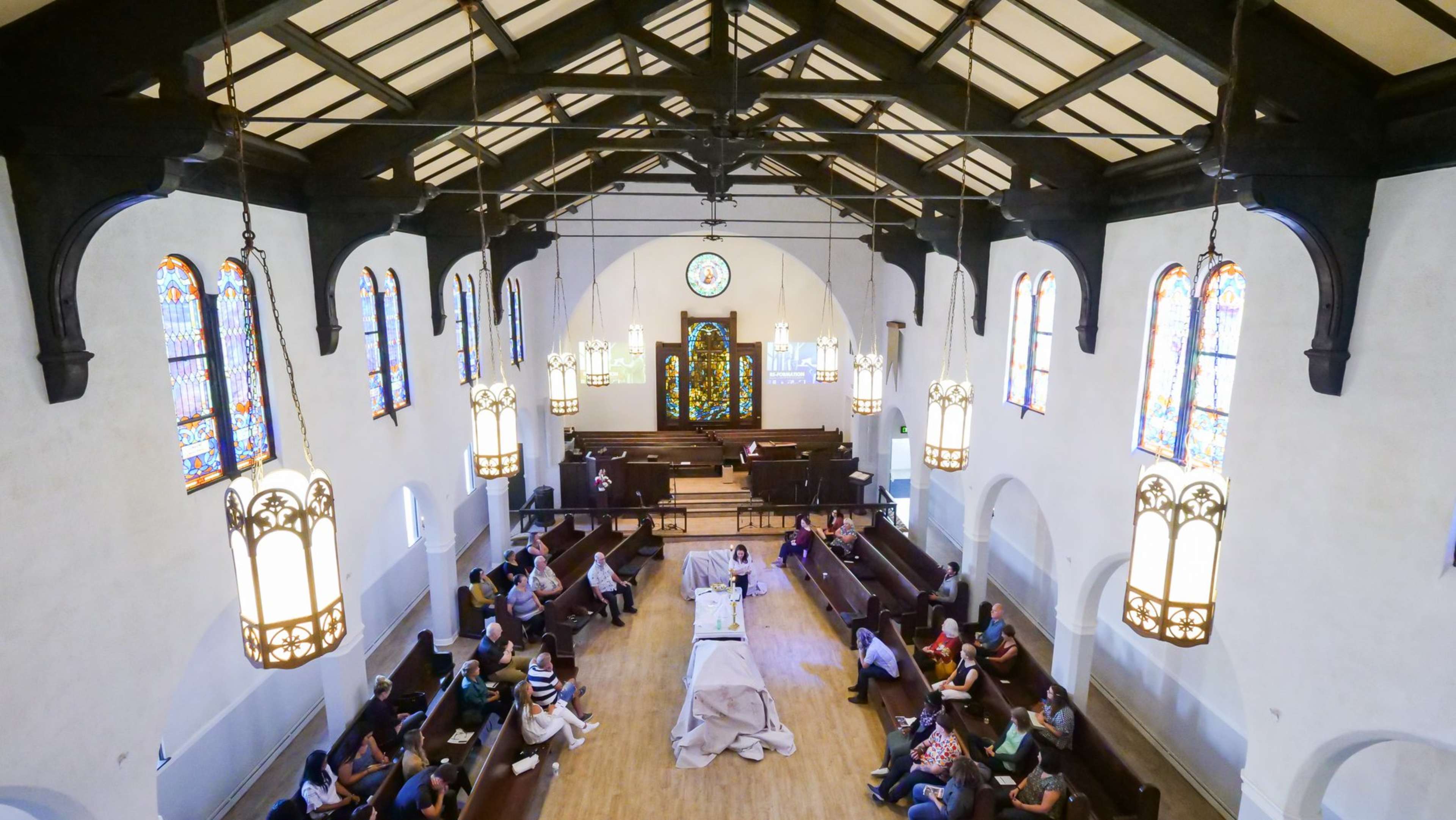 A spacious church interior with stained glass windows, featuring rows of seating and a central stage area where an event is taking place.