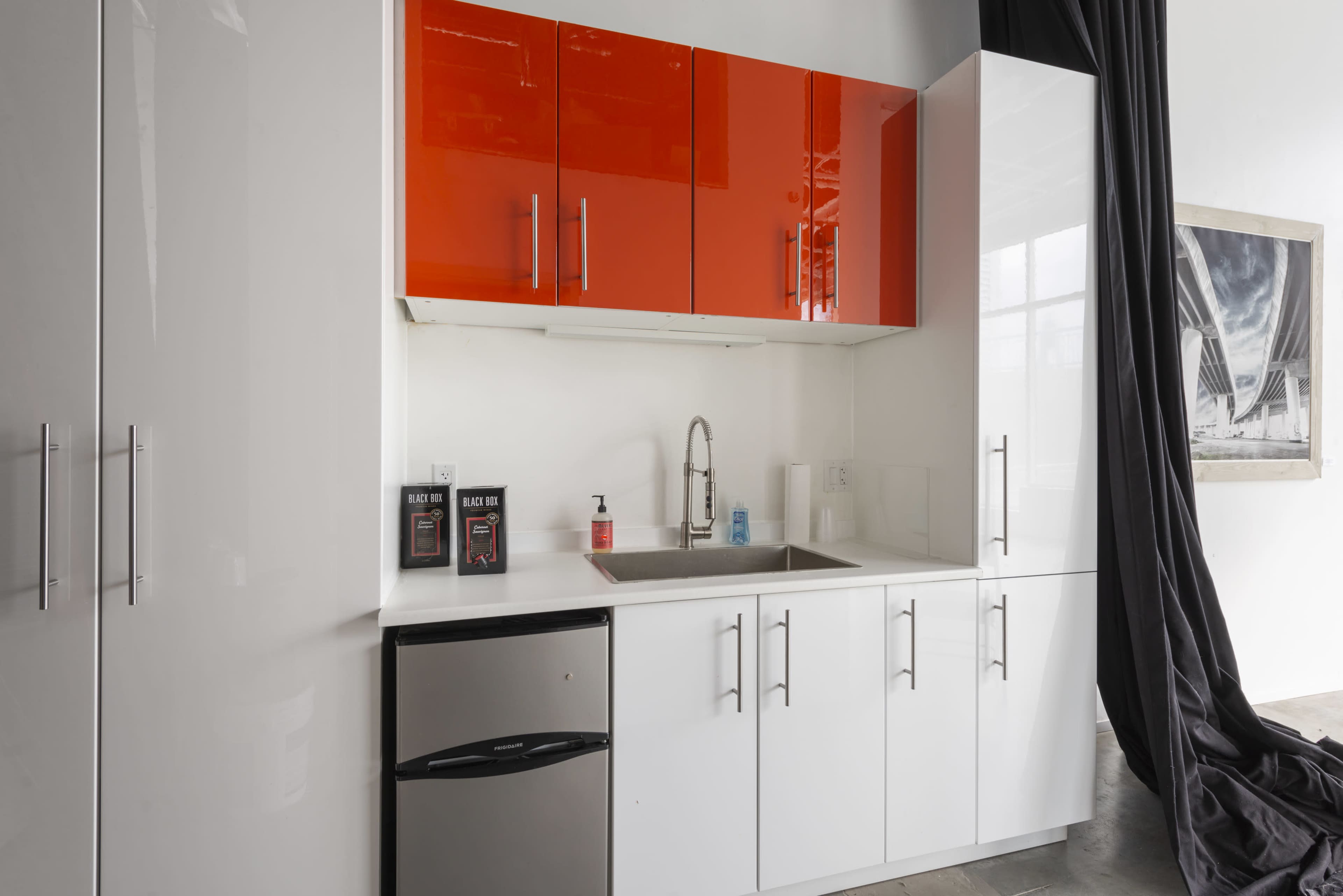 The image shows a modern kitchen with white cabinets, a stainless steel sink, and a small refrigerator.