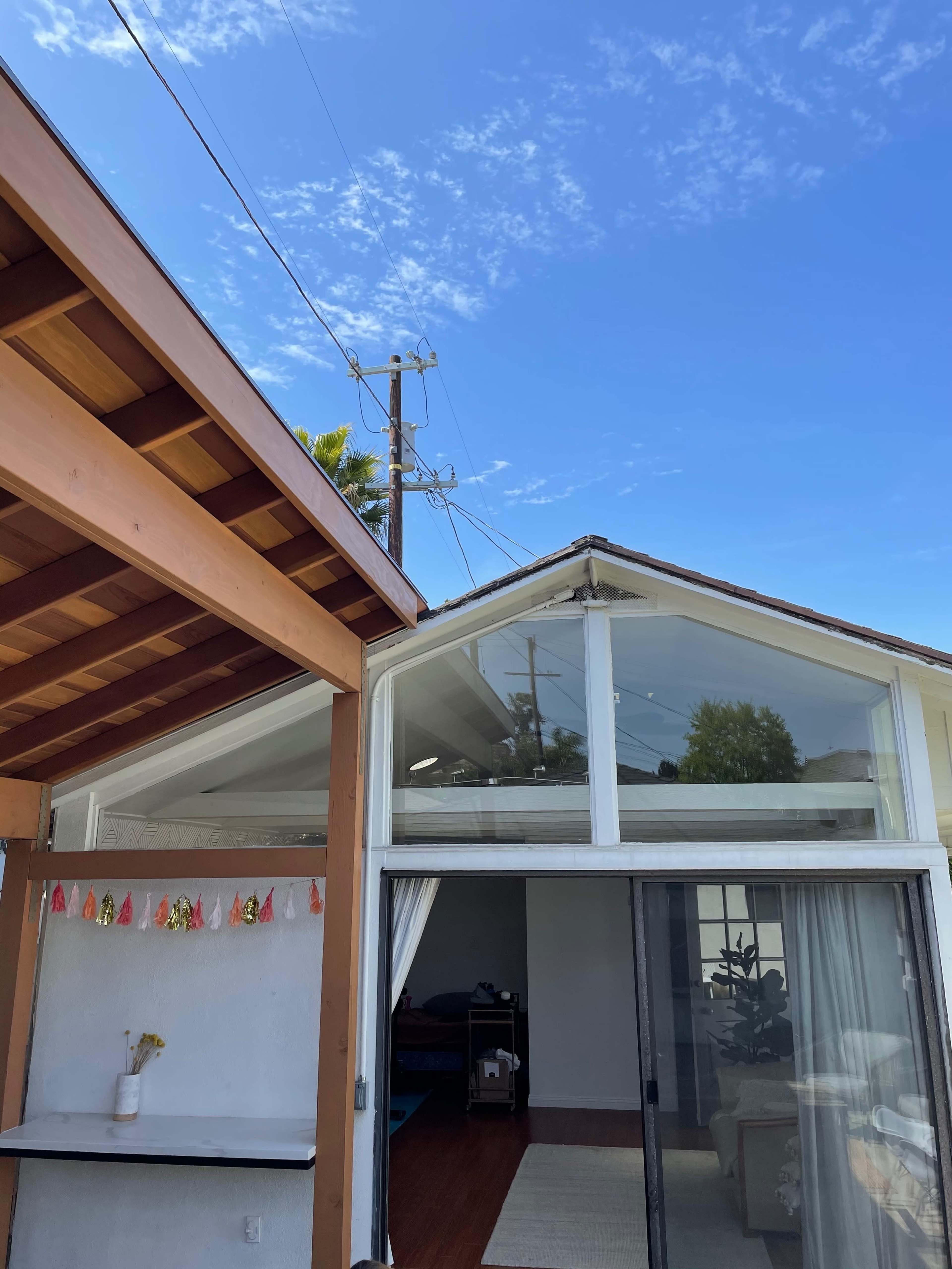 The image shows a clear blue sky above a house with a wooden structure on the left and a glass-panelled section on the right.