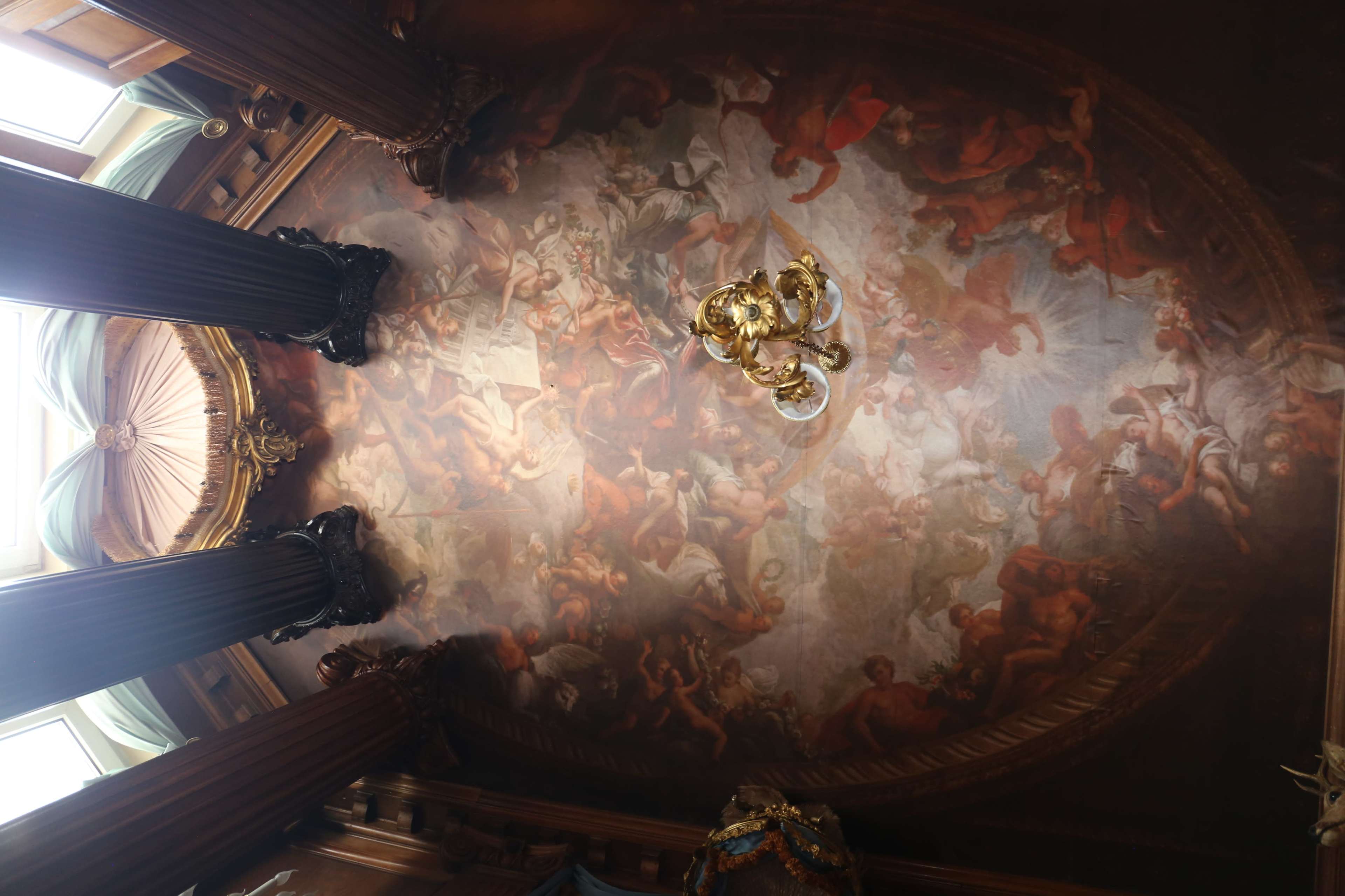 An ornate ceiling painted with classical figures and scenes, supported by decorative columns.