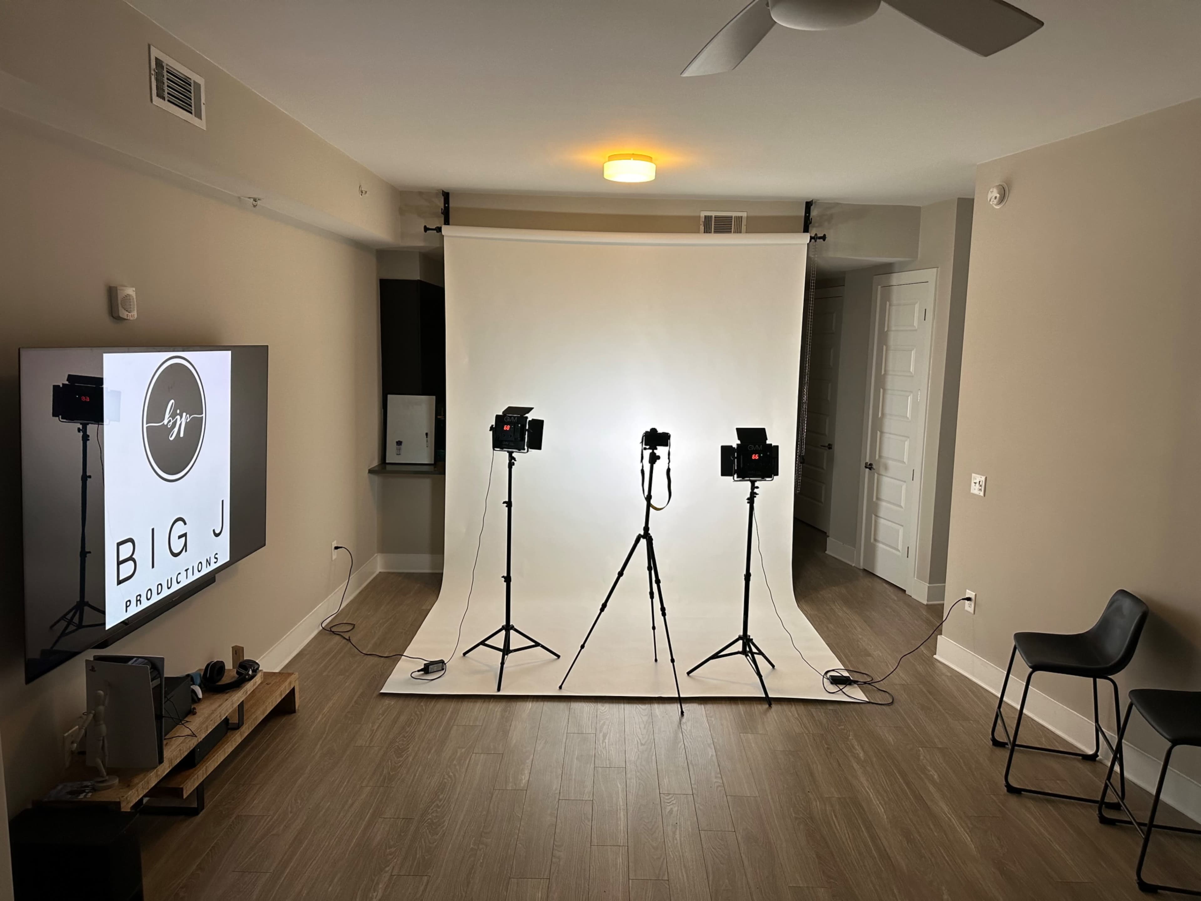 A studio setup with three tripods holding lights directed at a plain white backdrop in a minimalist room.