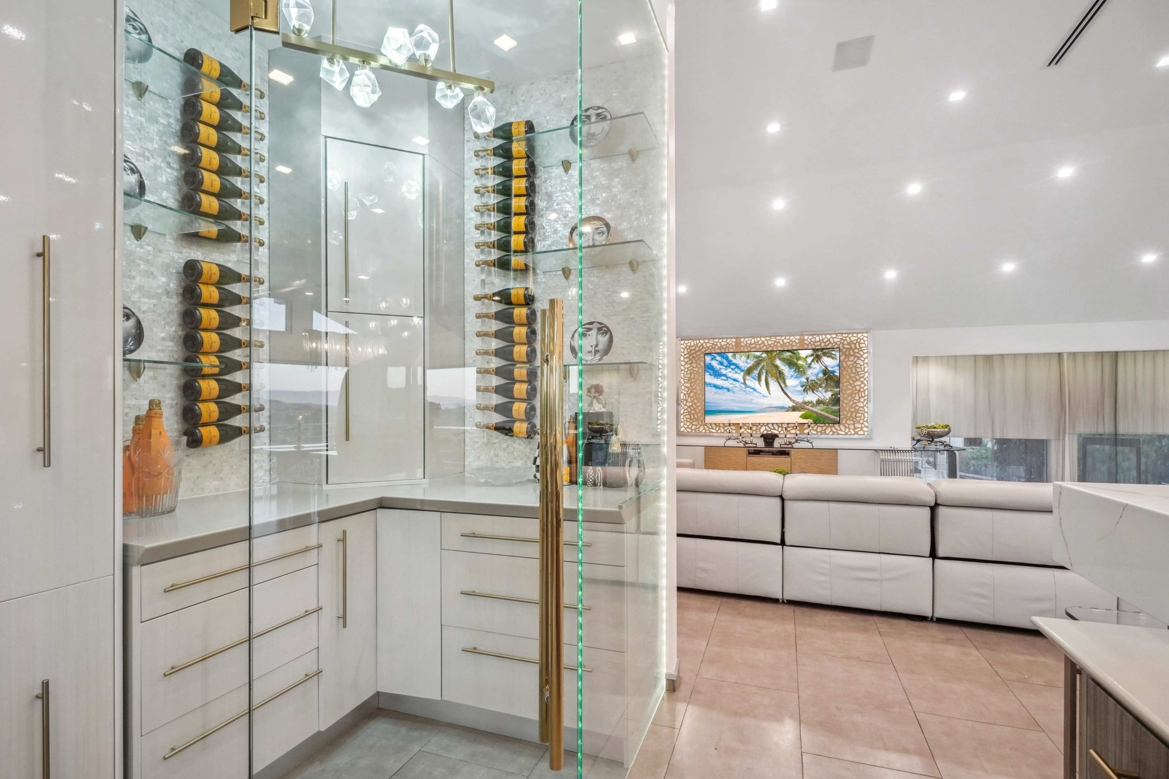 The image depicts a modern kitchen with a glass-enclosed wine display, showcasing bottles on a sleek wall-mounted rack, and an open living area in the background.