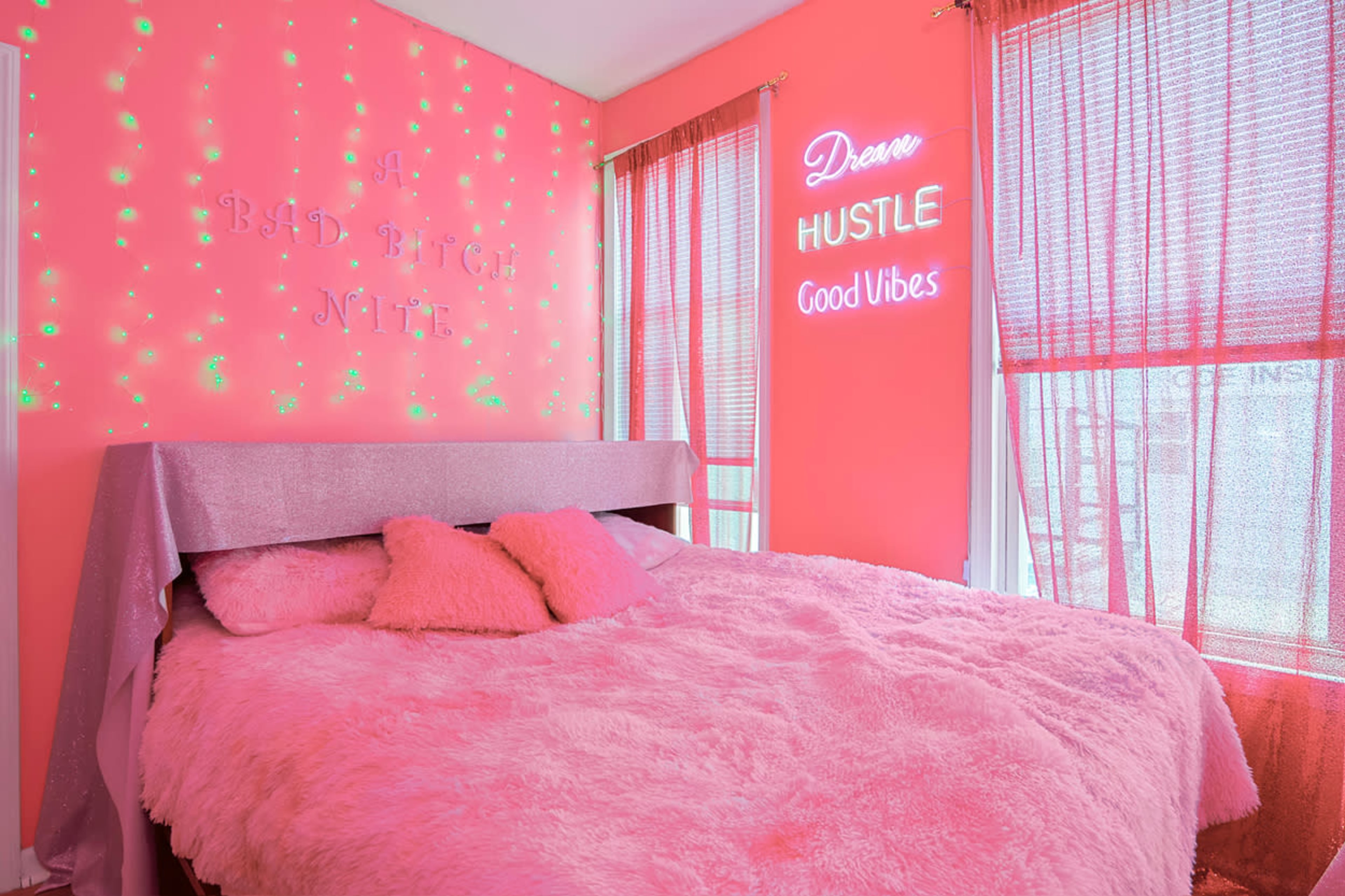 The room features a pink theme with a plush bed and neon signs on the walls.