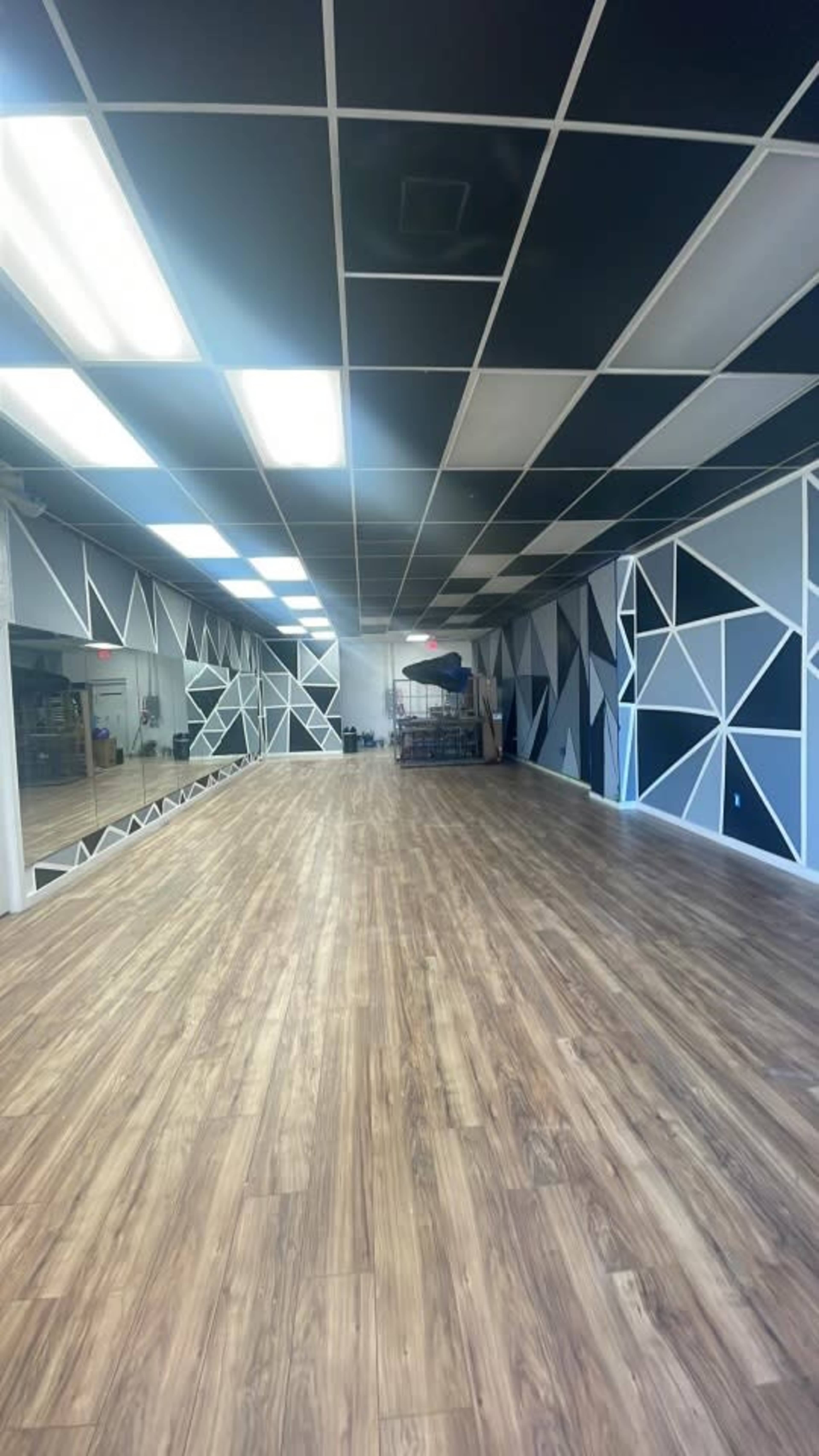 A spacious studio with a wooden floor, black and white geometric patterns on the walls, and bright overhead lighting.