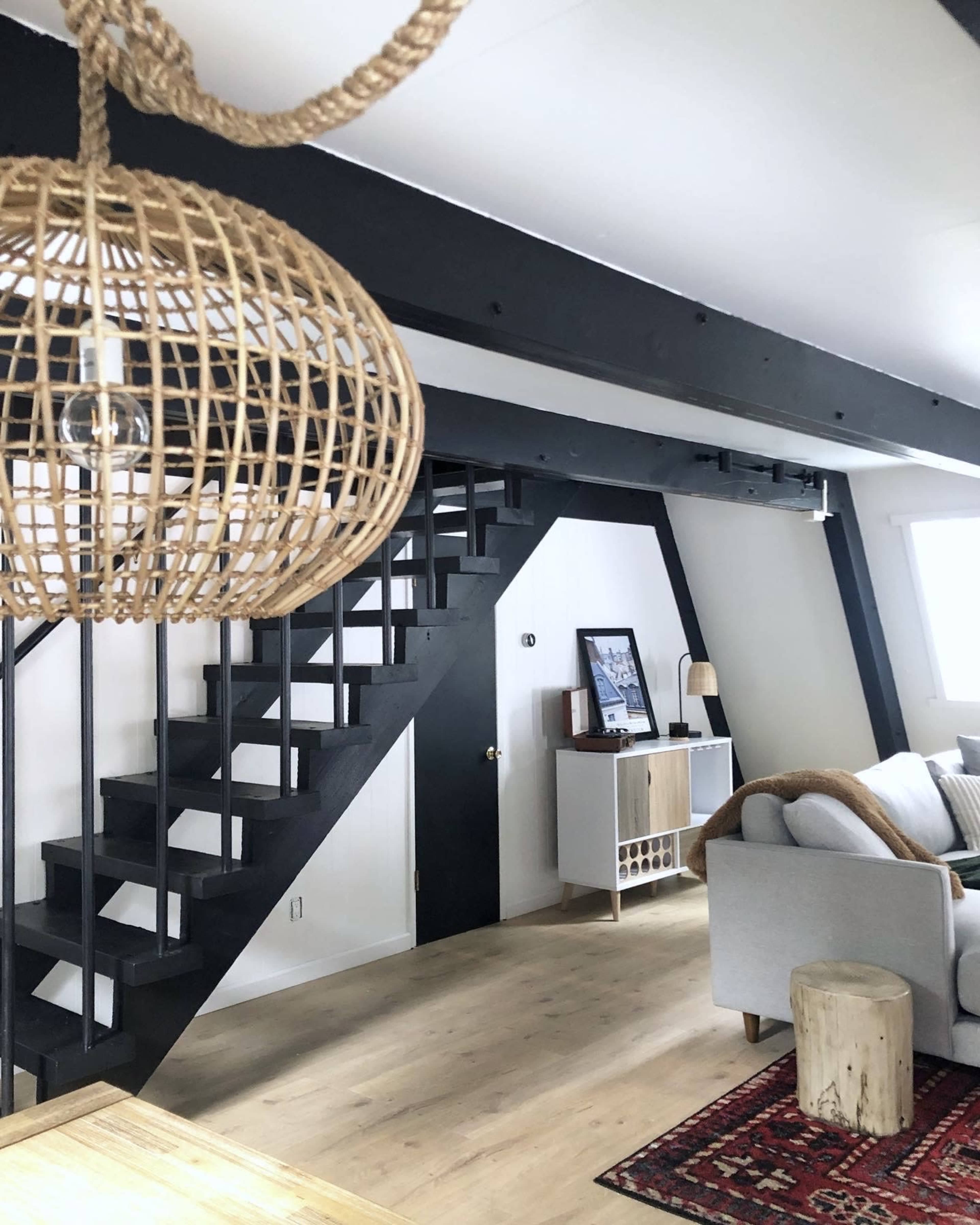 A modern interior with a black staircase leading to a loft, accompanied by a woven light fixture and a neatly arranged living space.