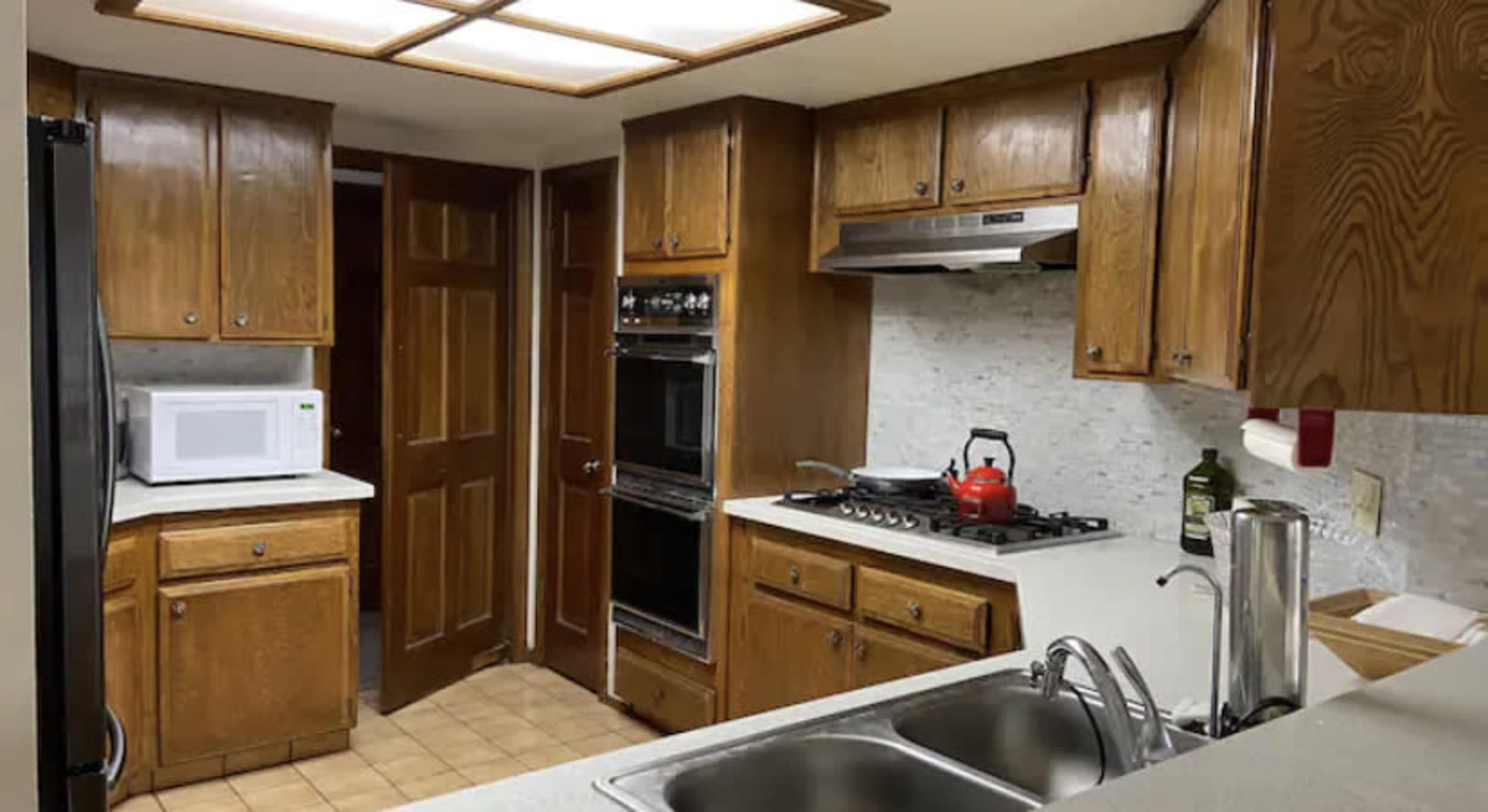 A kitchen with wooden cabinets, a double sink, an oven, a stovetop, and a microwave on the counter.
