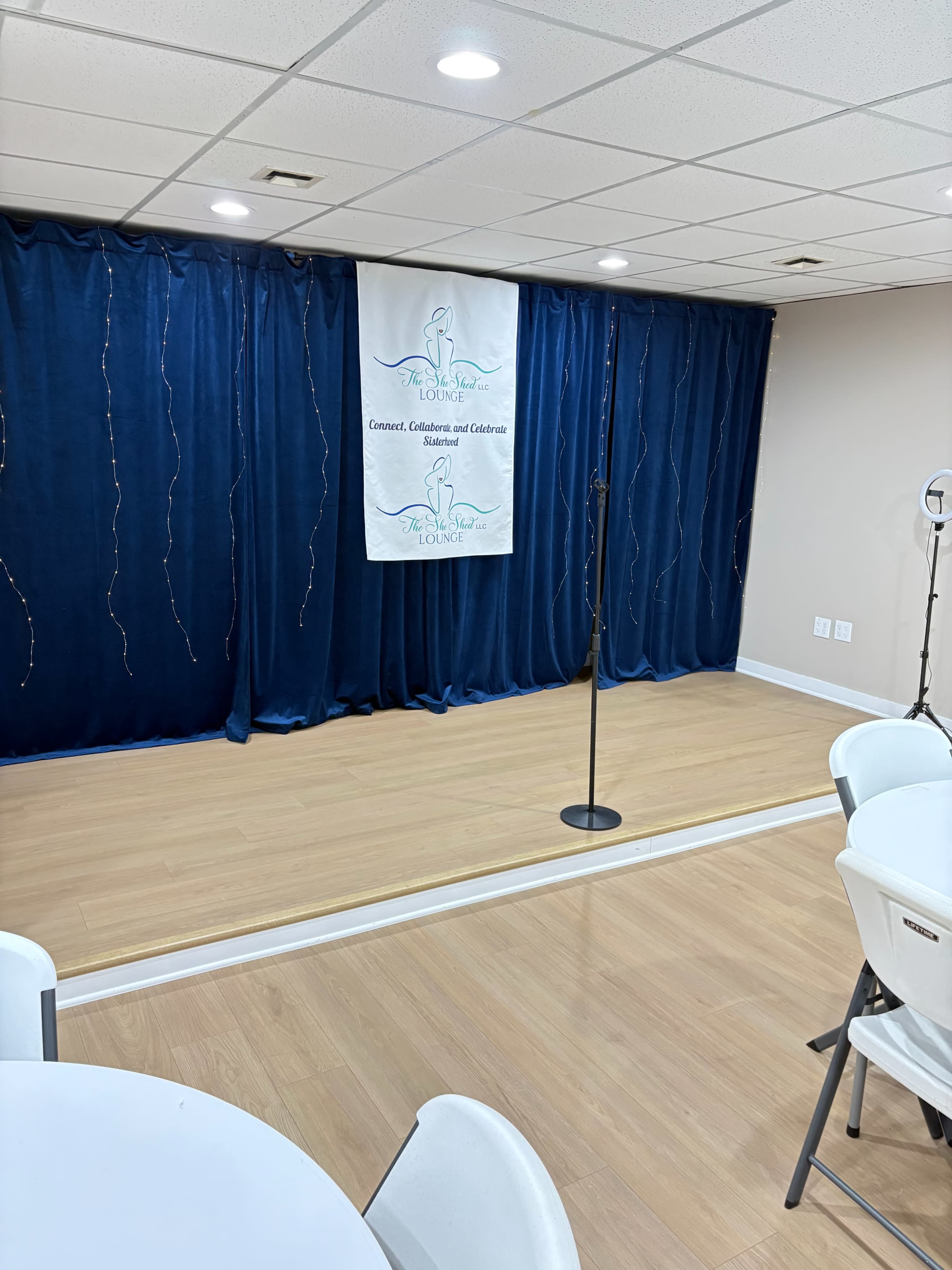 The image shows a small stage with a microphone and a blue curtain backdrop, adorned with a banner for an event titled "LOOPA: Concert, Collaboration, and Celebration."