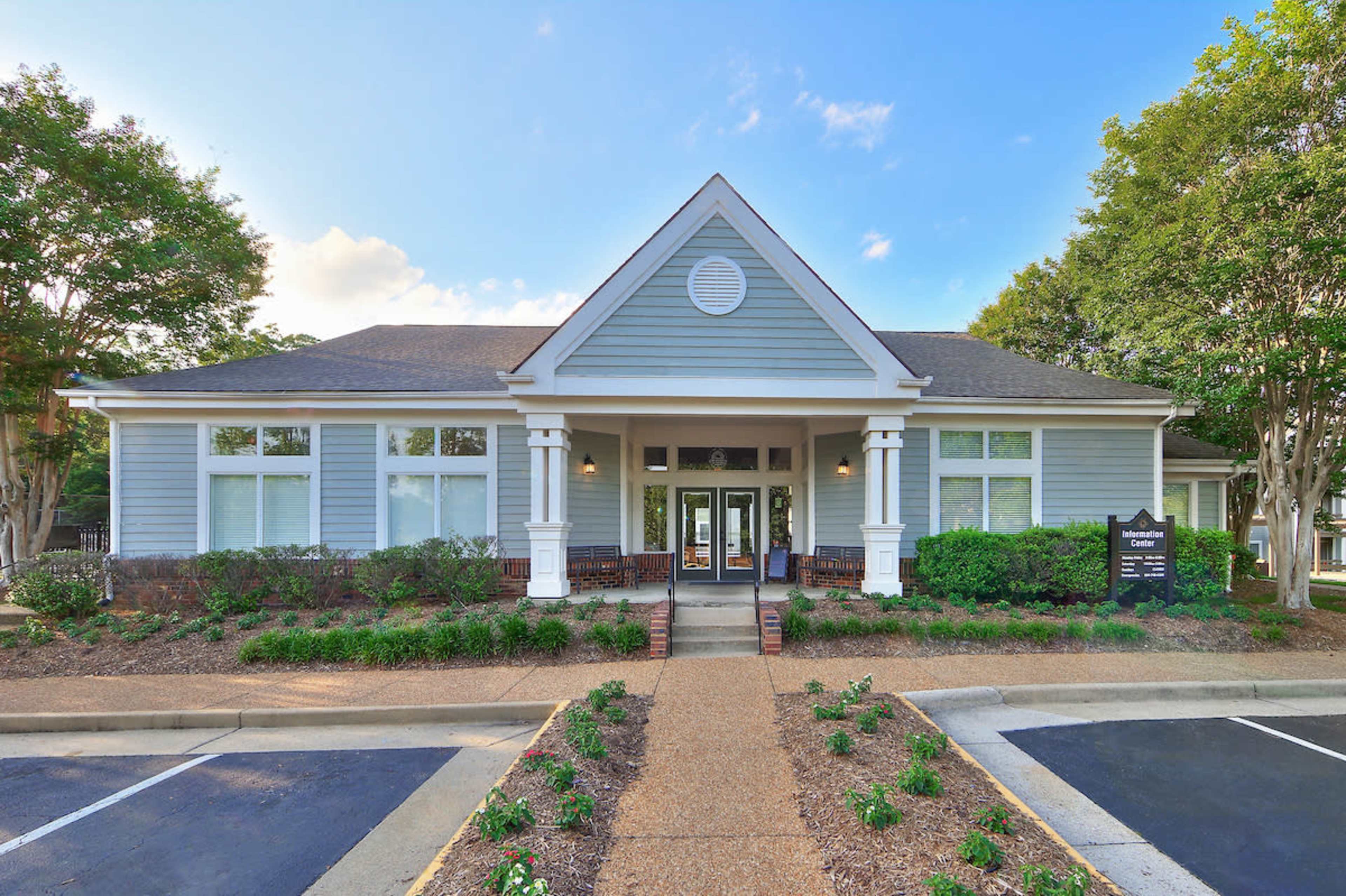 A light blue building with a triangular roof, large front windows, and landscaped greenery surrounding the entrance.