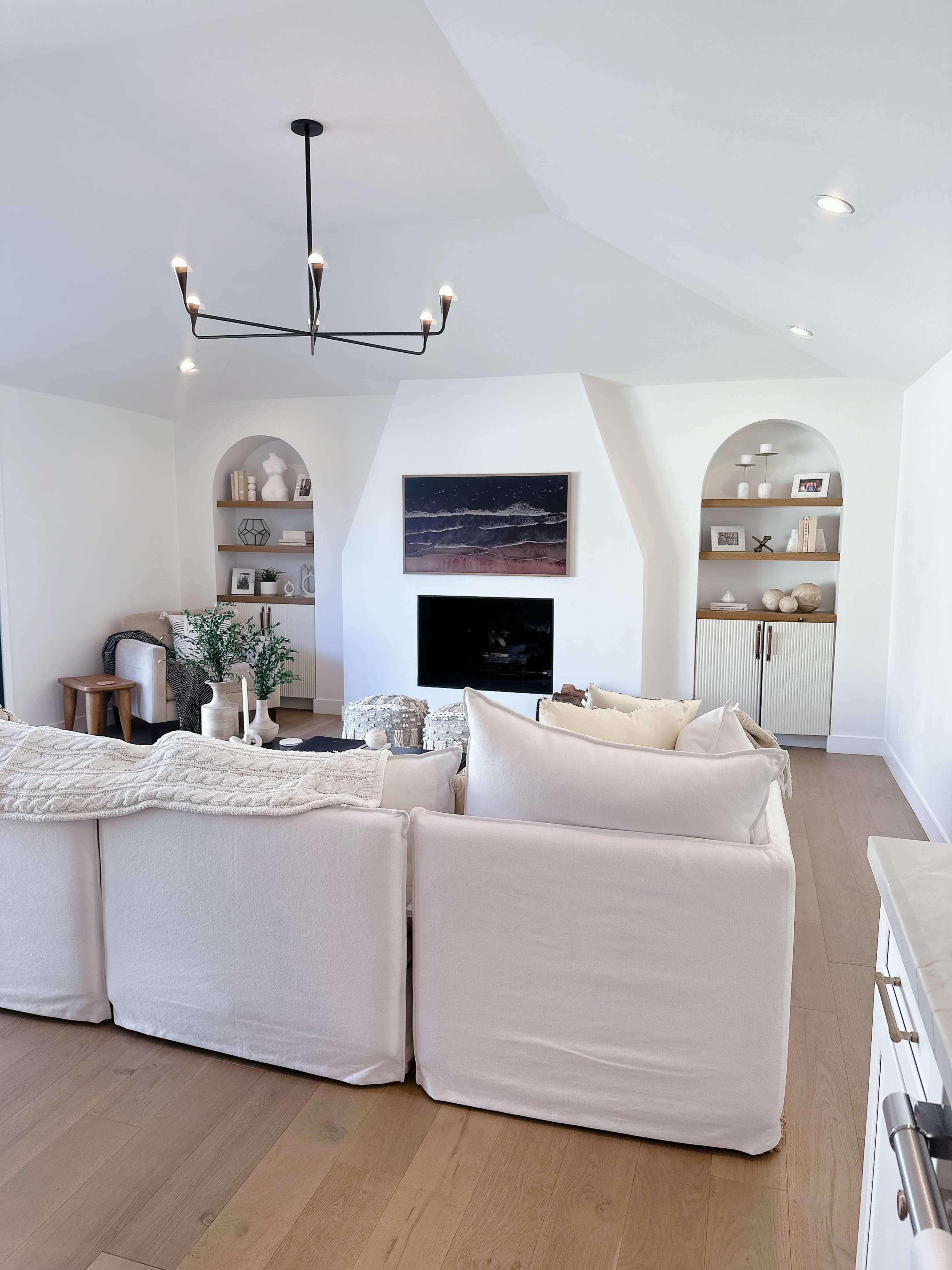 A modern living room with white walls, a ceiling light fixture, a large sofa, a fireplace, and built-in shelves displaying decorative items.