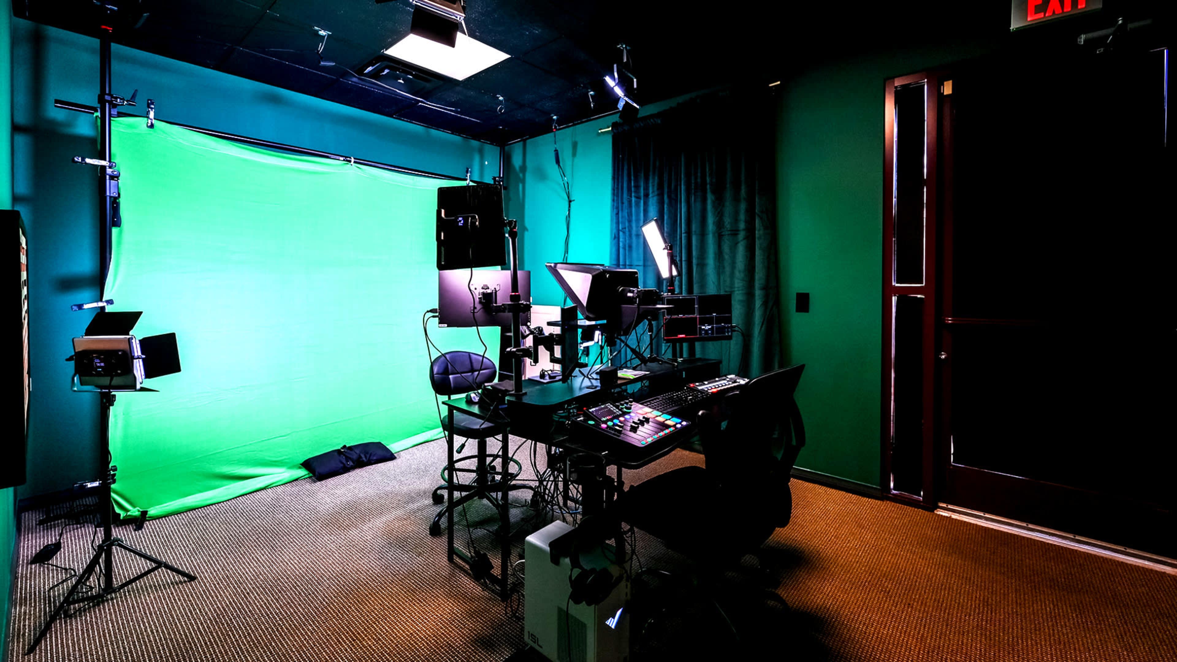 The image shows a media studio with a green screen backdrop, equipped with lighting and a control desk with various recording equipment.