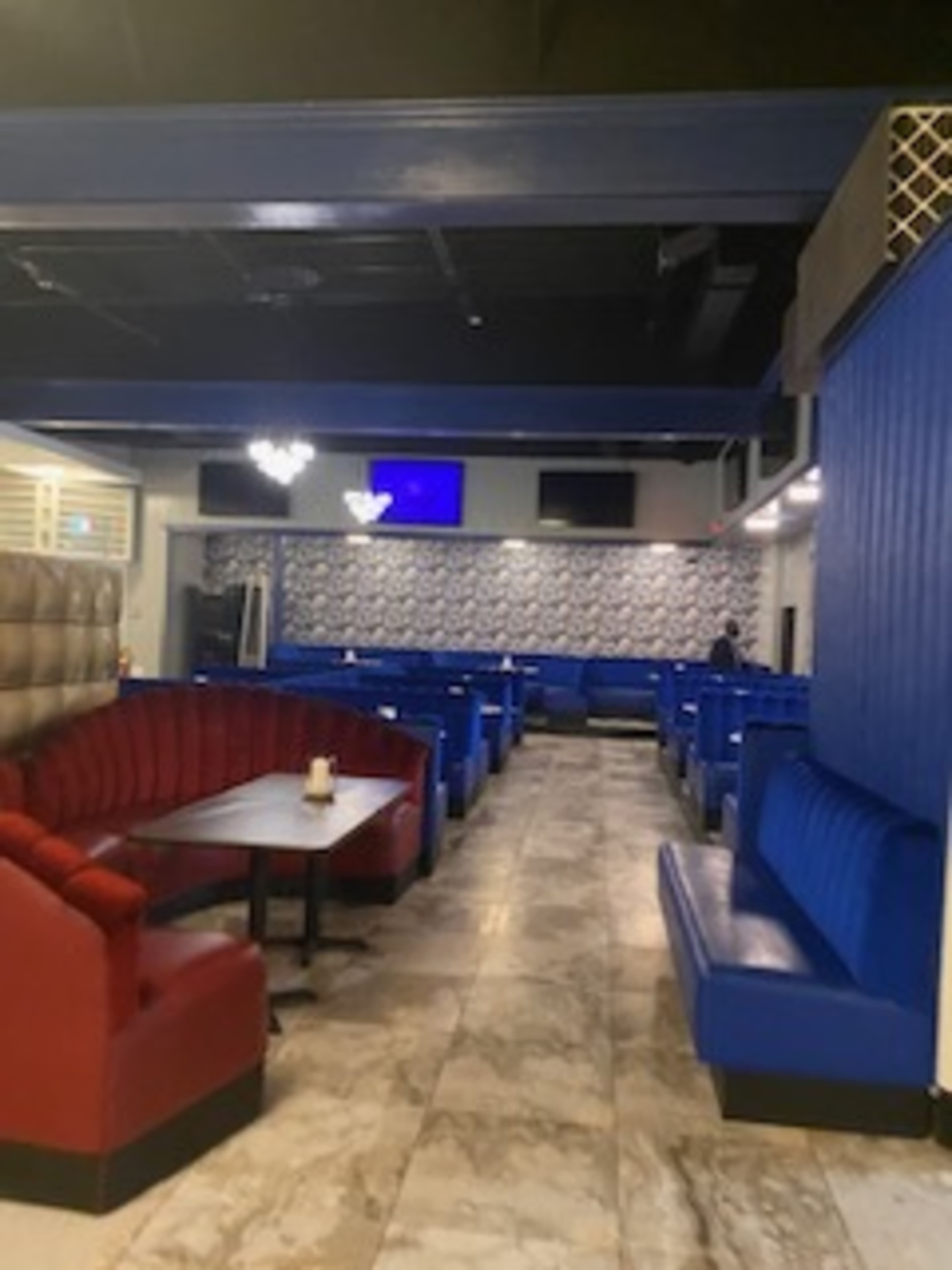 The image shows a modern interior of a restaurant with blue and red seating booths arranged around tables on a marble floor.