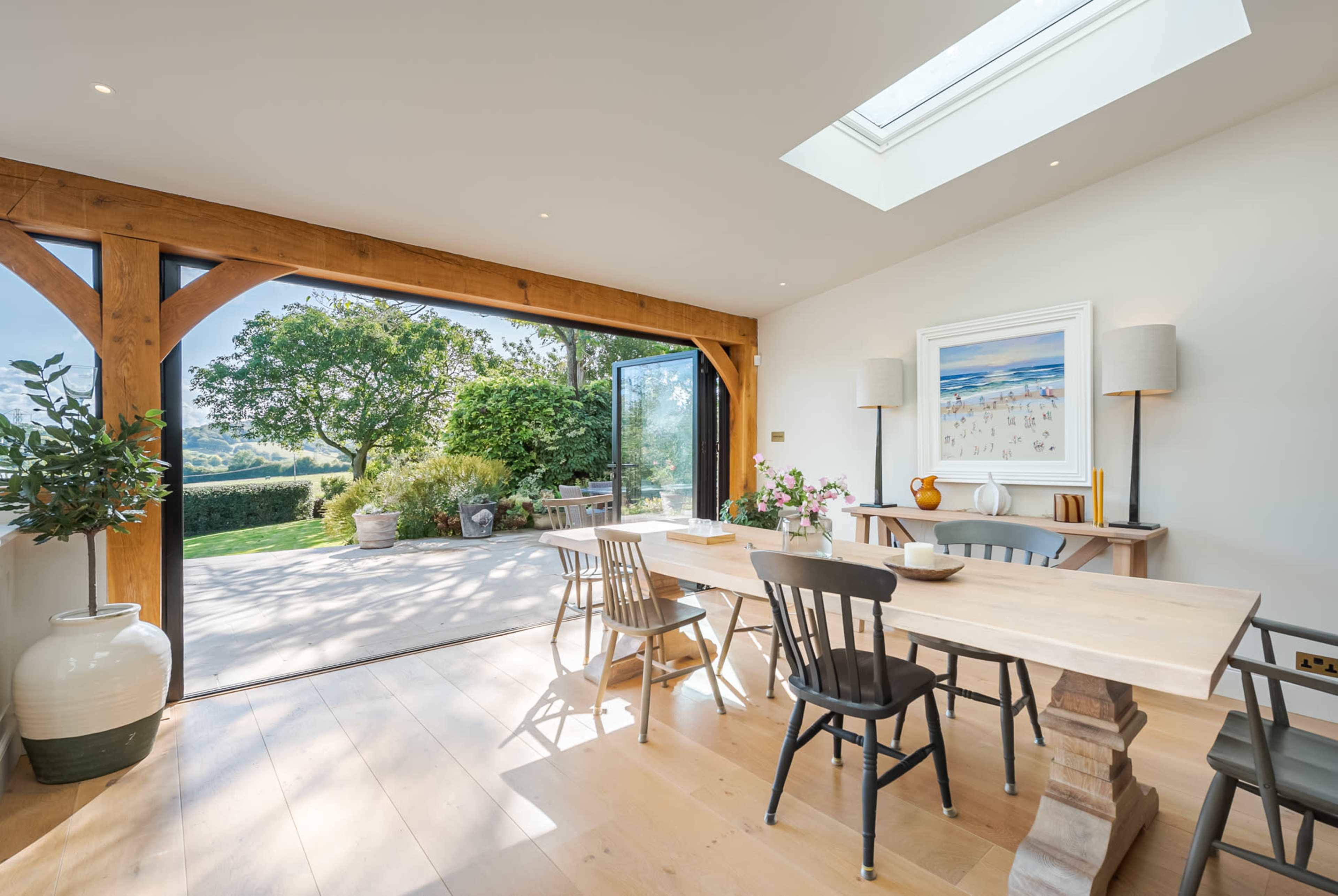 A bright dining area features a wooden table surrounded by chairs, with large glass doors opening to a scenic outdoor view.