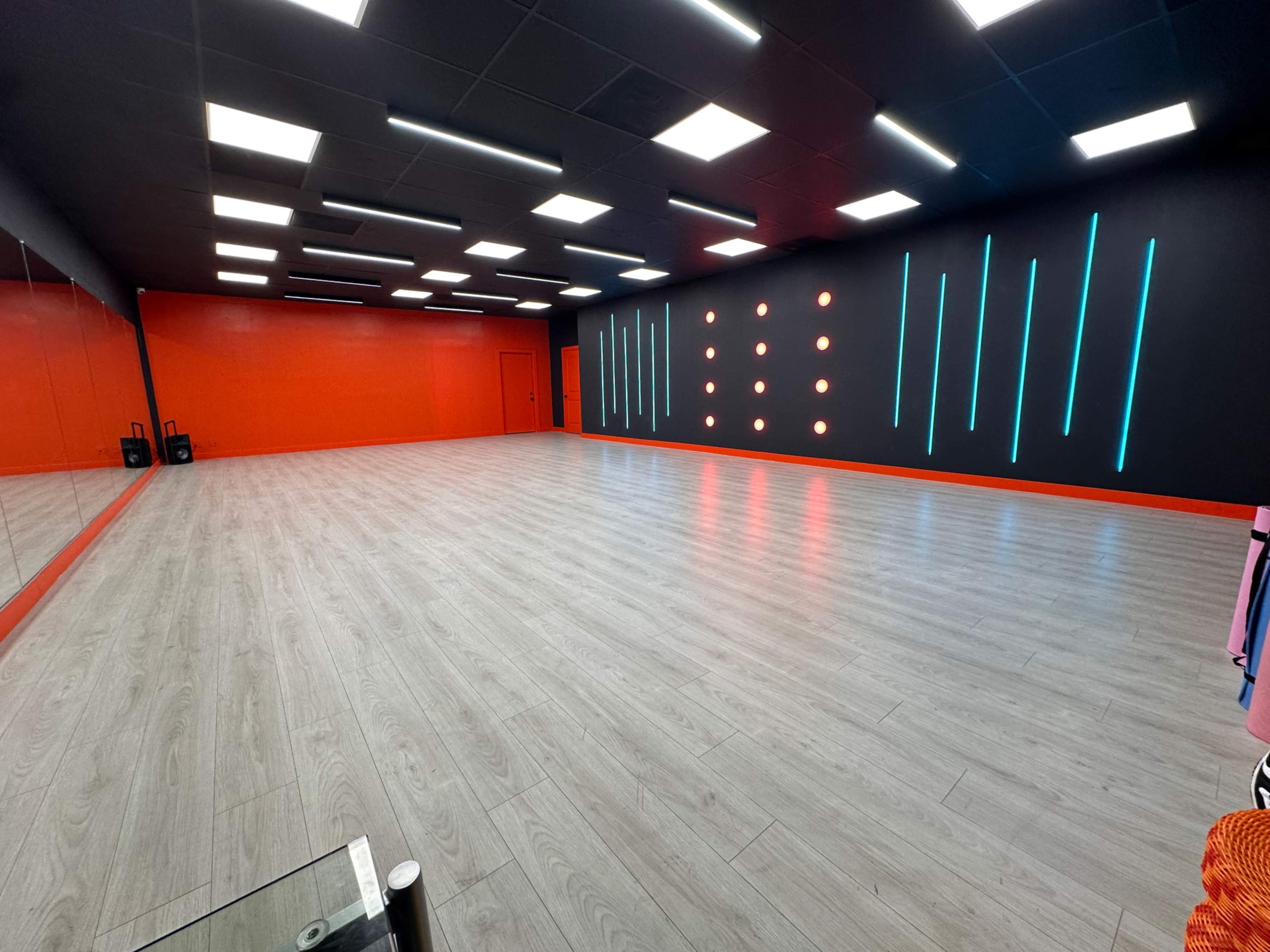 A spacious dance studio with wooden flooring, red and black walls, and illuminated accent lighting.