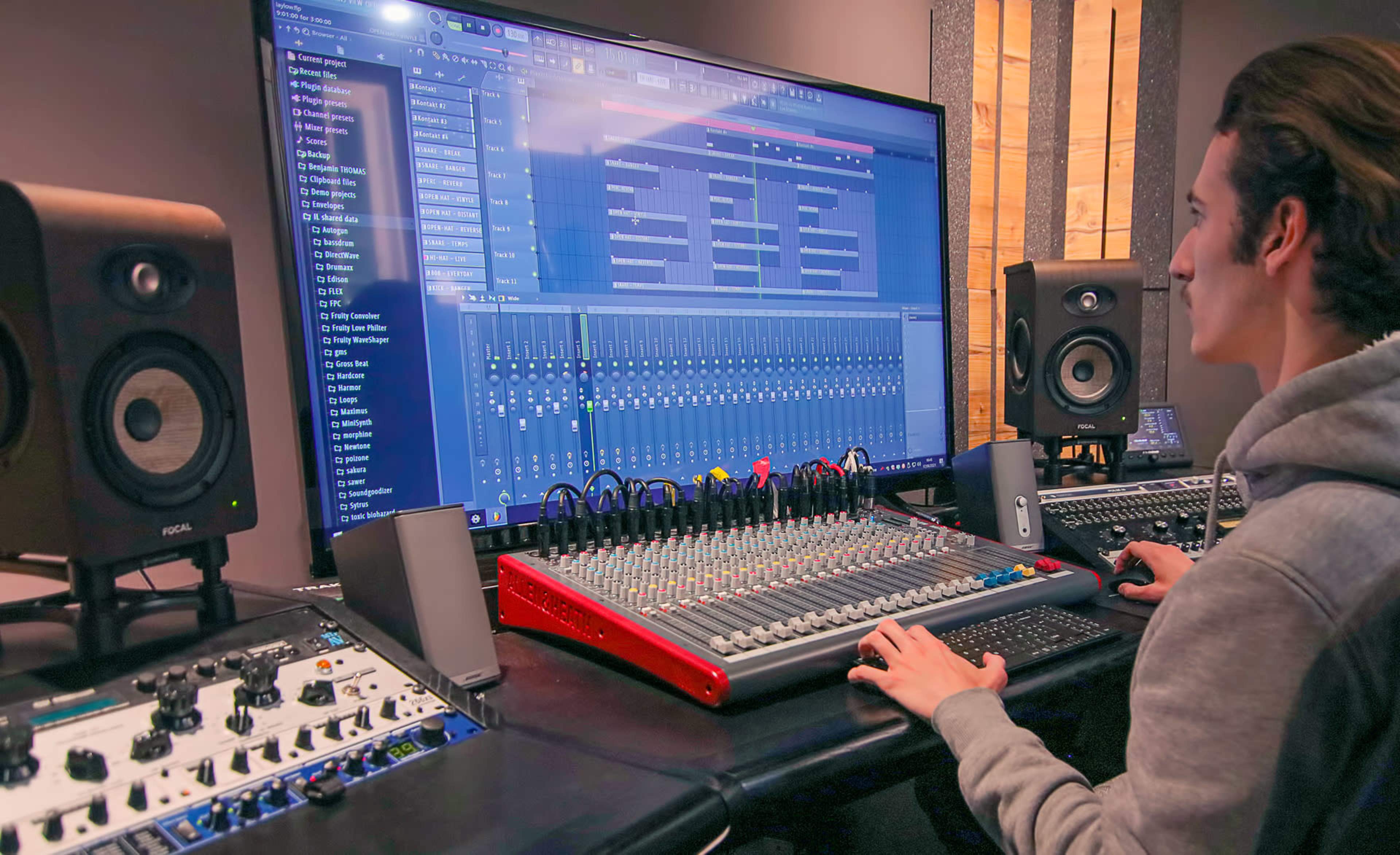 A person operates a digital audio workstation on a large screen while using a mixing console in a music studio.