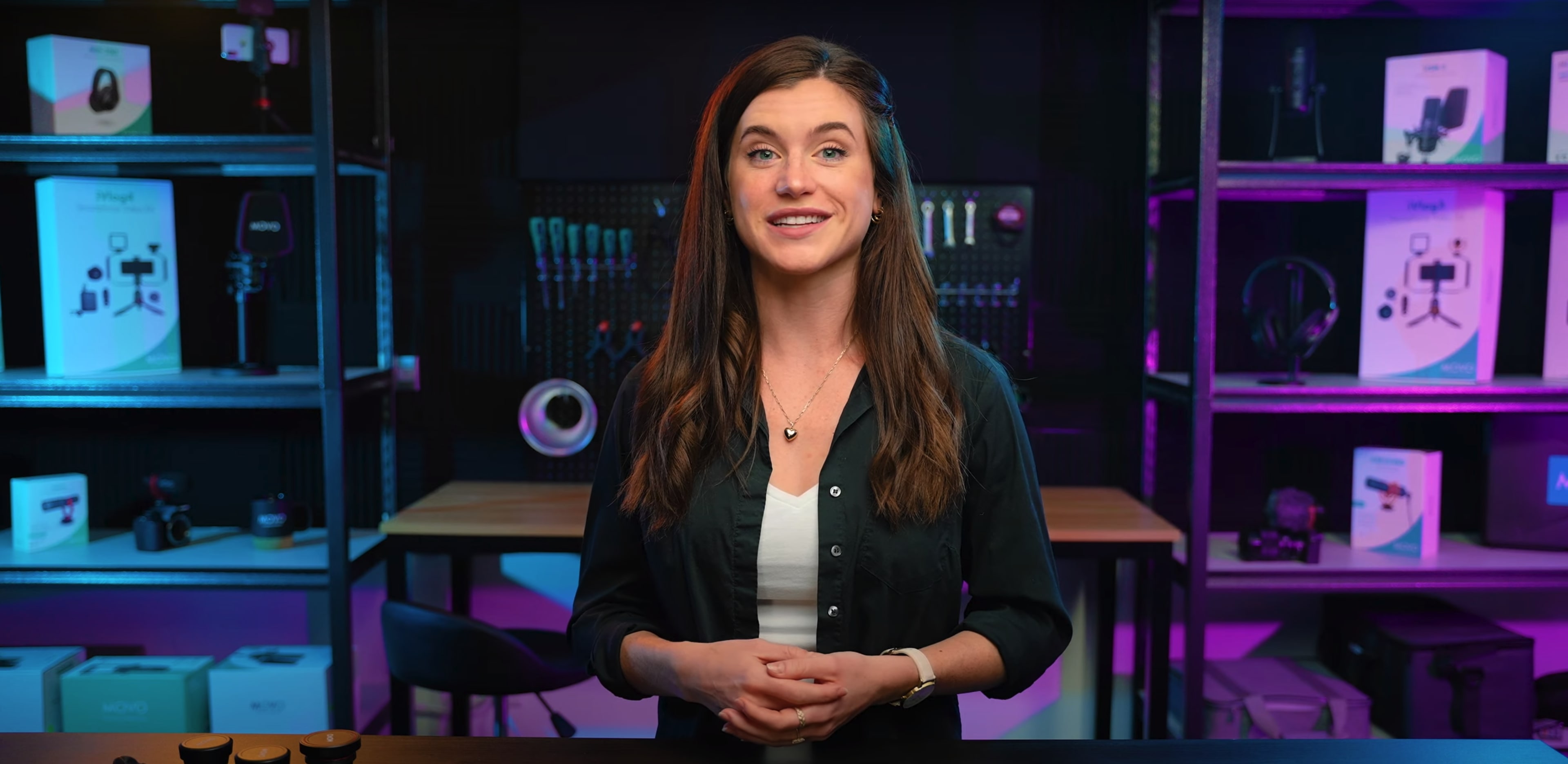 A woman stands in front of a shelf filled with various audio and video equipment, smiling at the camera.