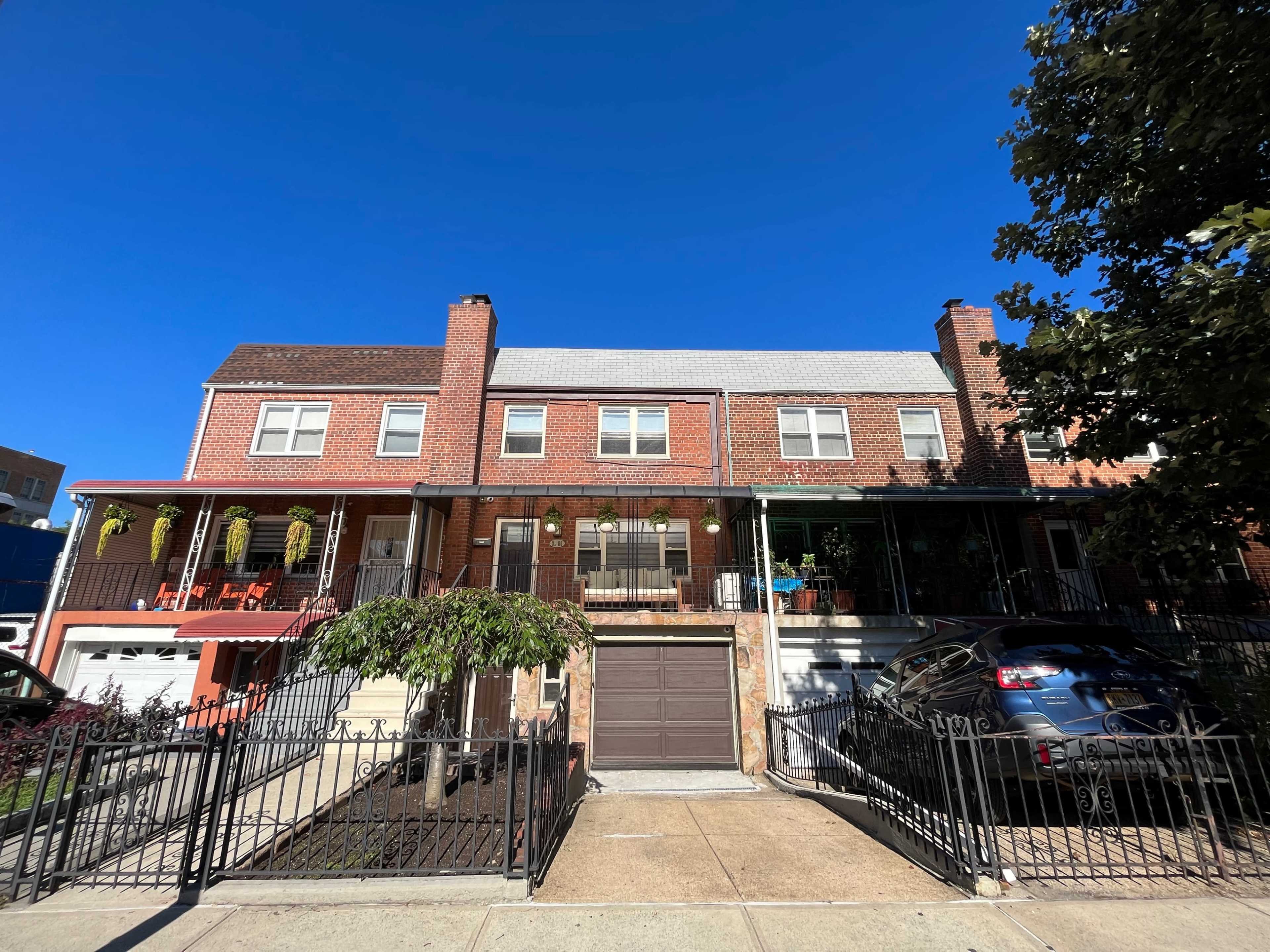 The image shows a row of two-story brick houses with front porches and a driveway, set against a clear blue sky.