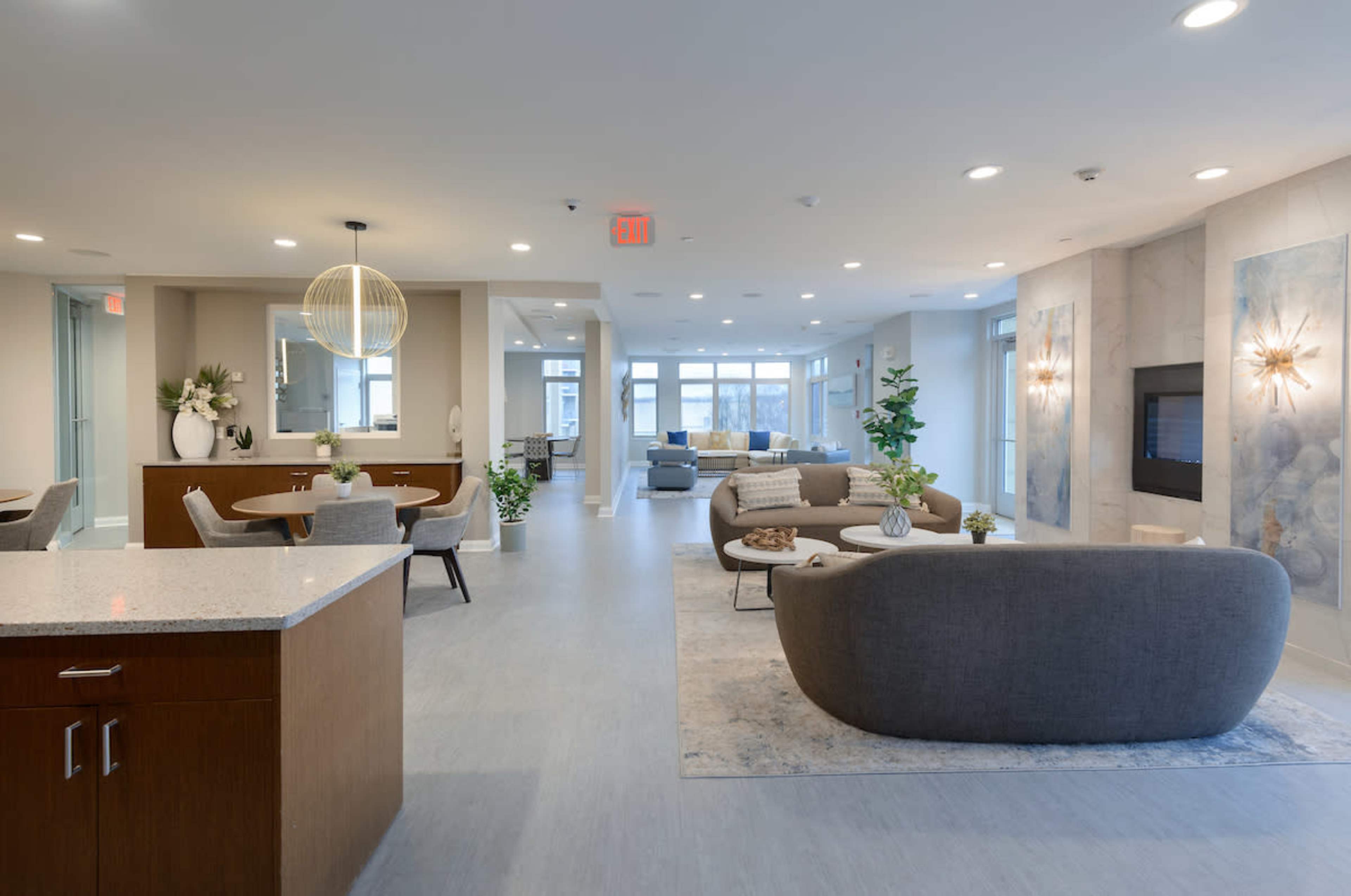 A modern lounge and dining area featuring a kitchen island, seating arrangements, and large windows.