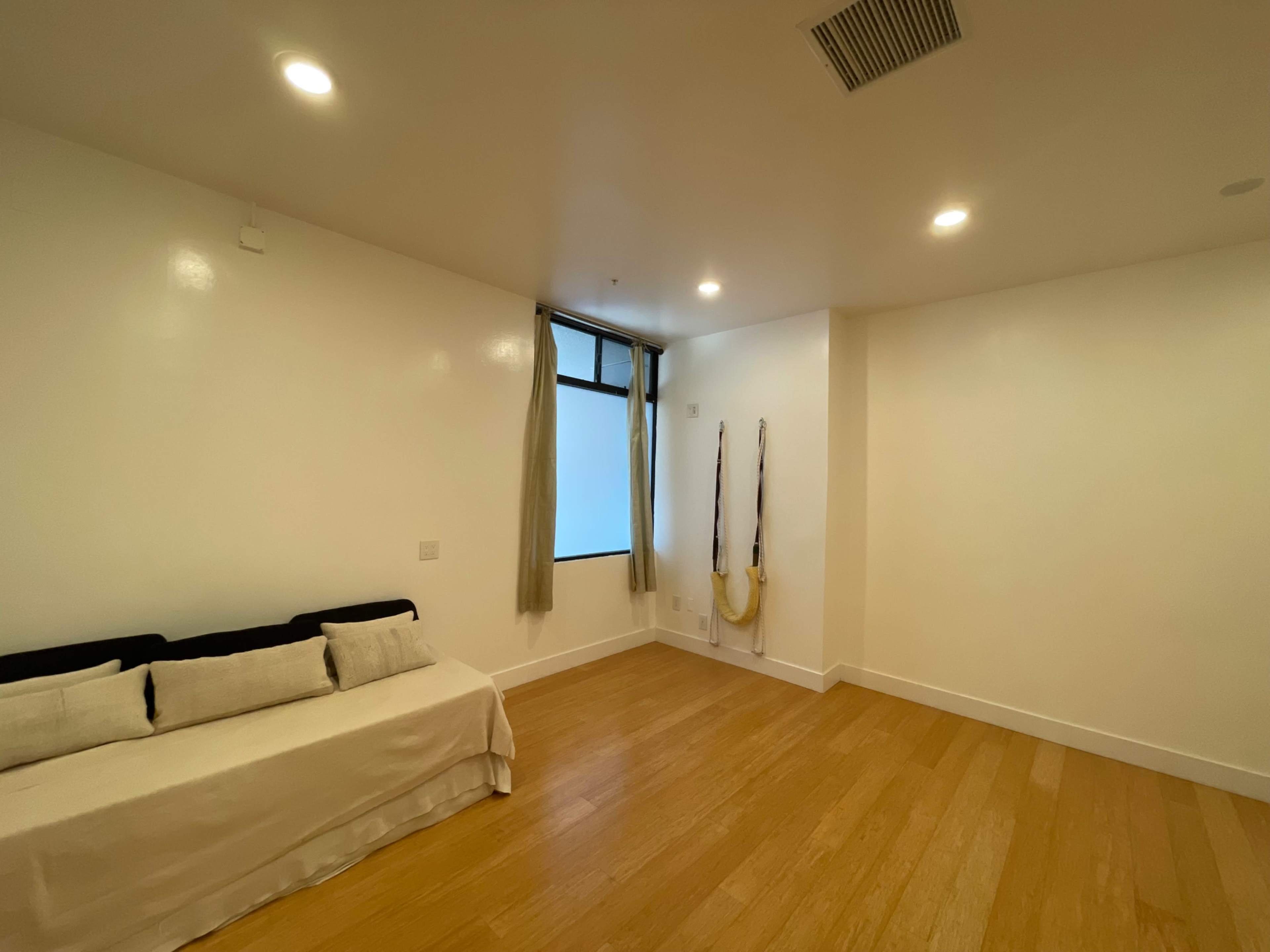 A sparsely furnished room with a light-colored floor, a sofa against one wall, and a window with curtains.