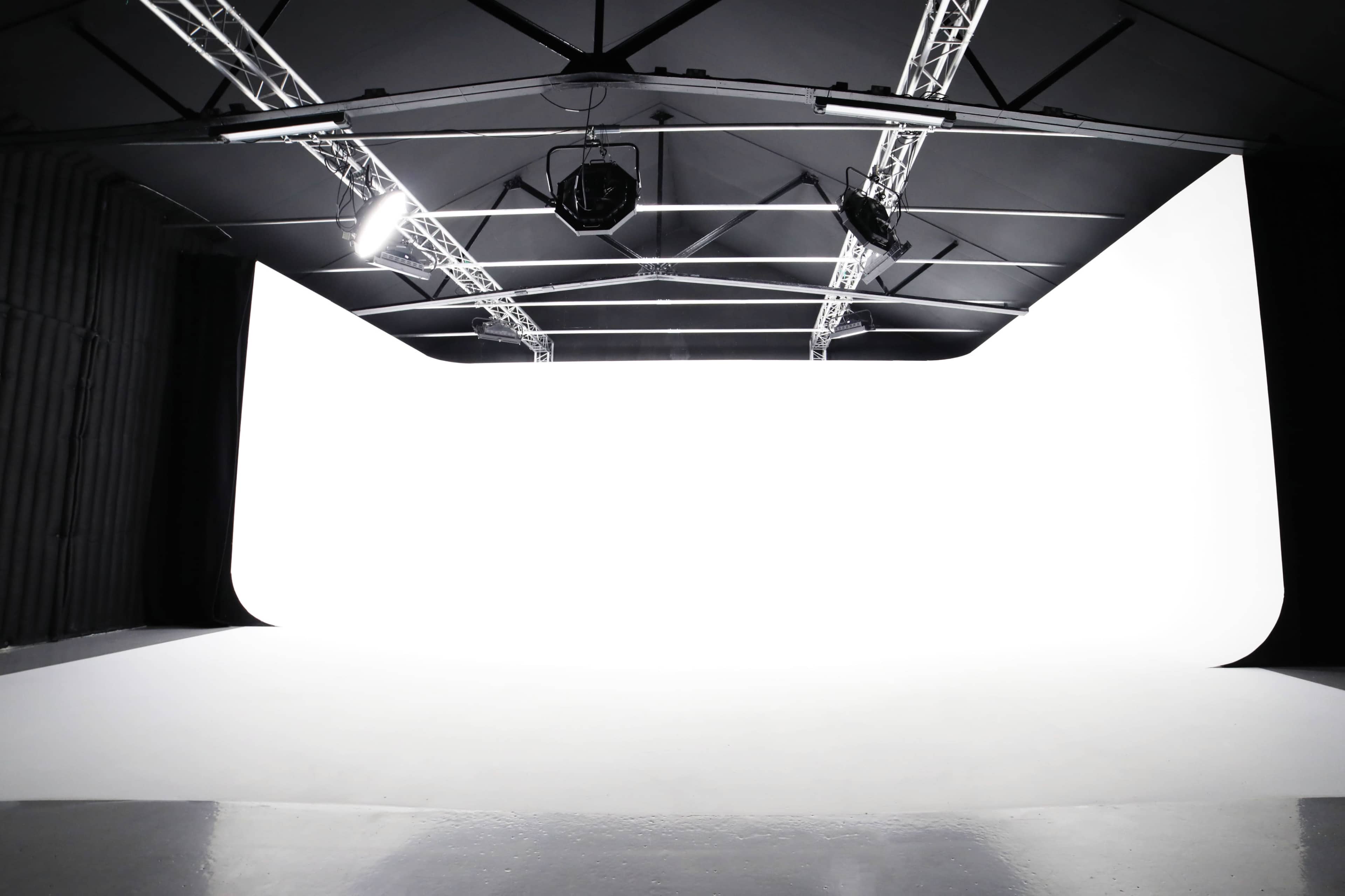 A spacious studio with a white backdrop, suspended lights, and a smooth floor.