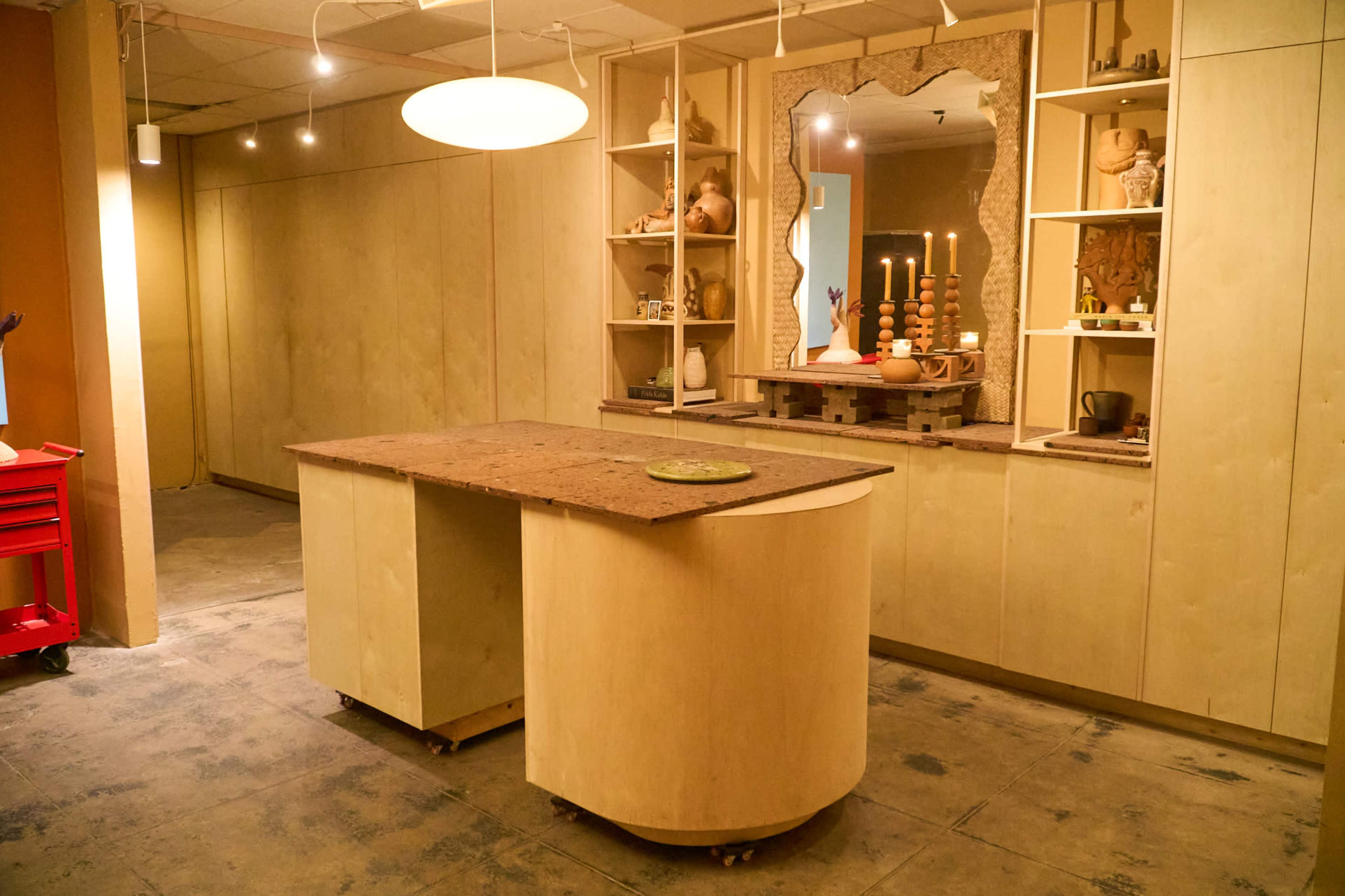 The image shows a spacious interior with wooden walls, an island countertop on wheels, shelves displaying various items, and candles set on a table.